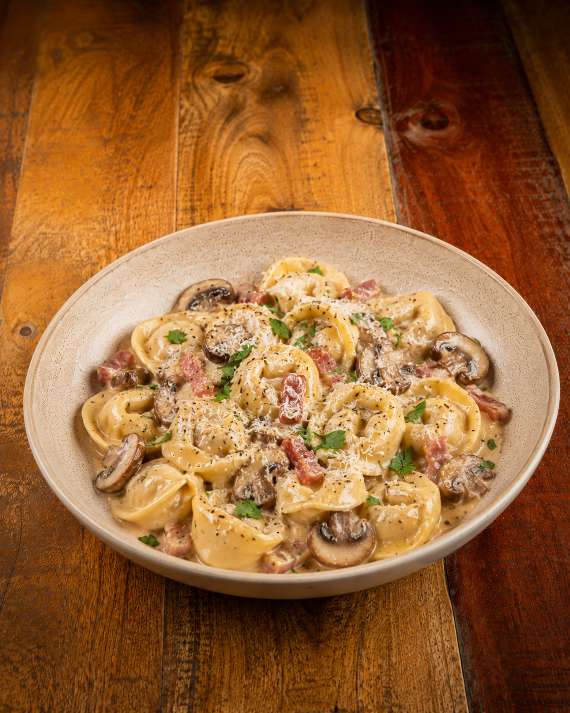 A bowl of creamy pasta with mushrooms, bacon, and parsley on a wooden table.