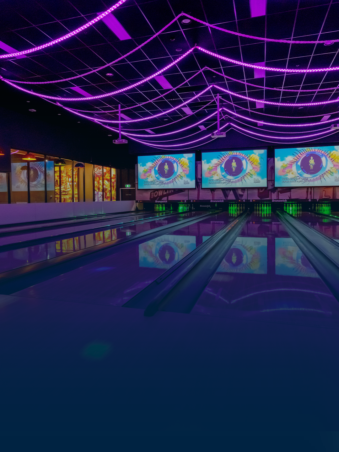 A bowling alley with purple neon lights on the ceiling and large digital screens displaying colorful eye graphics.