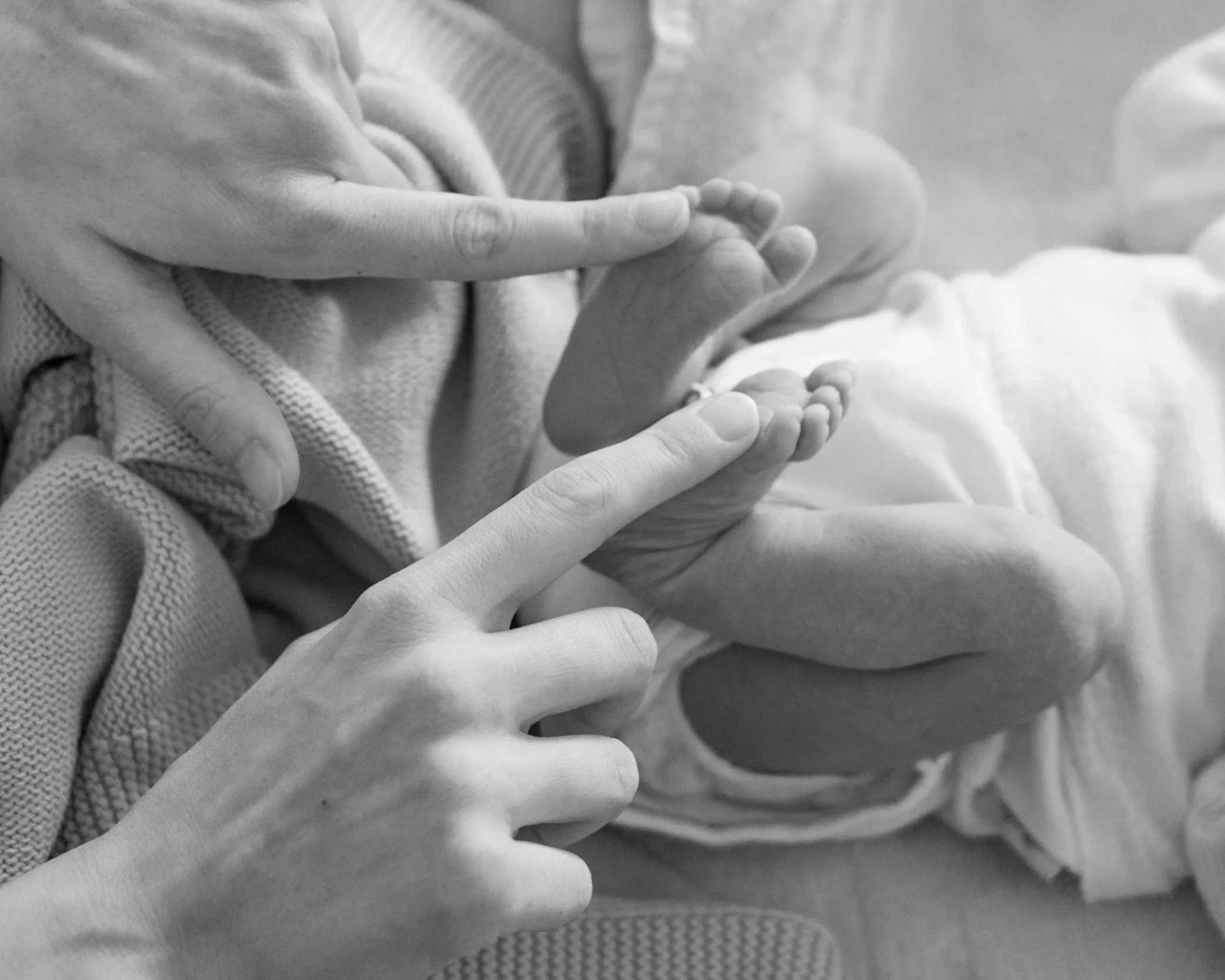 Black and white photo of a mother's hands gently holding a baby’s feet.