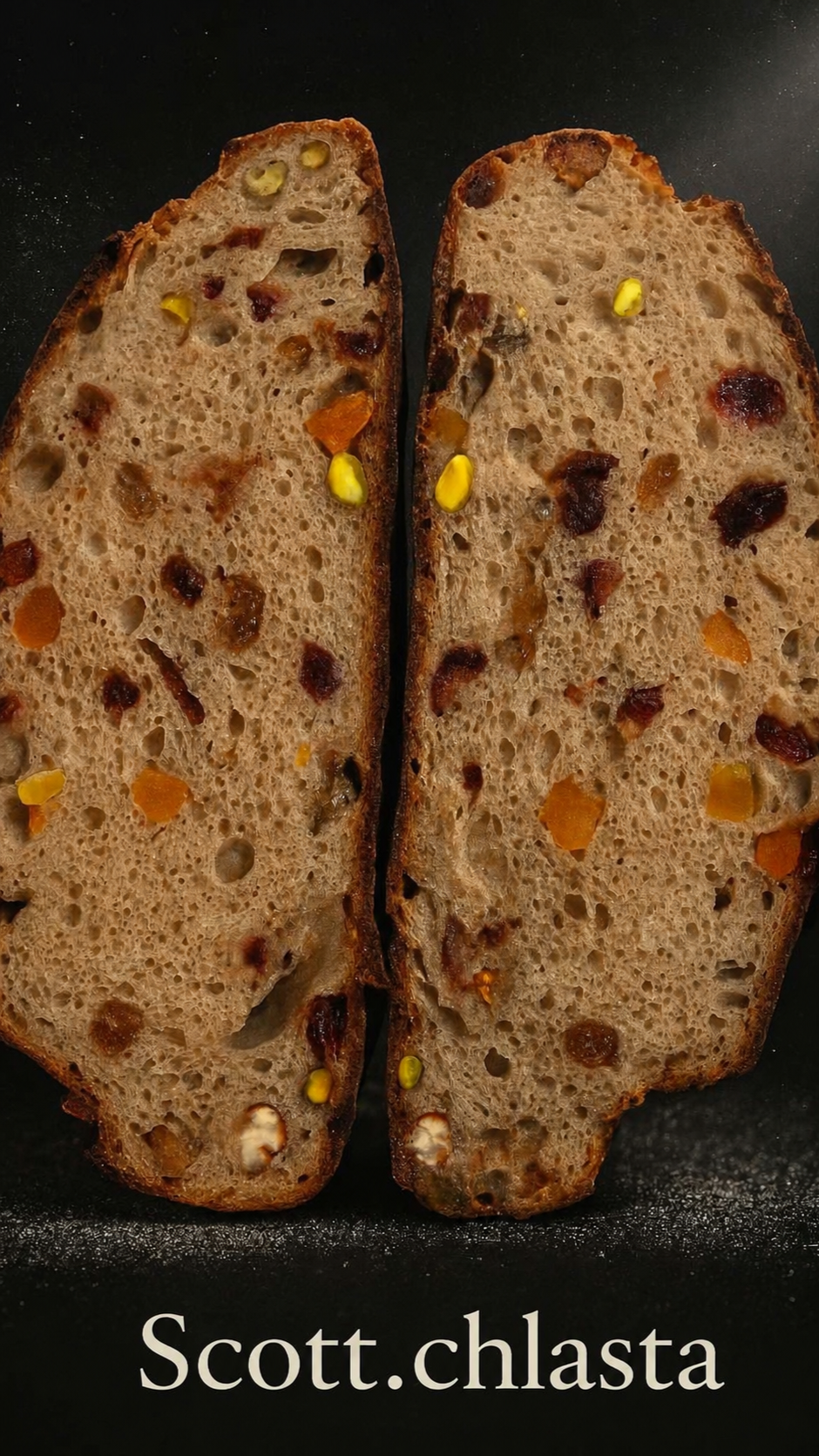 Deux tranches de pain aux fruits secs, avec des morceaux de fruits confits, sur un fond noir, avec la mention 'scott.chasta' en bas.