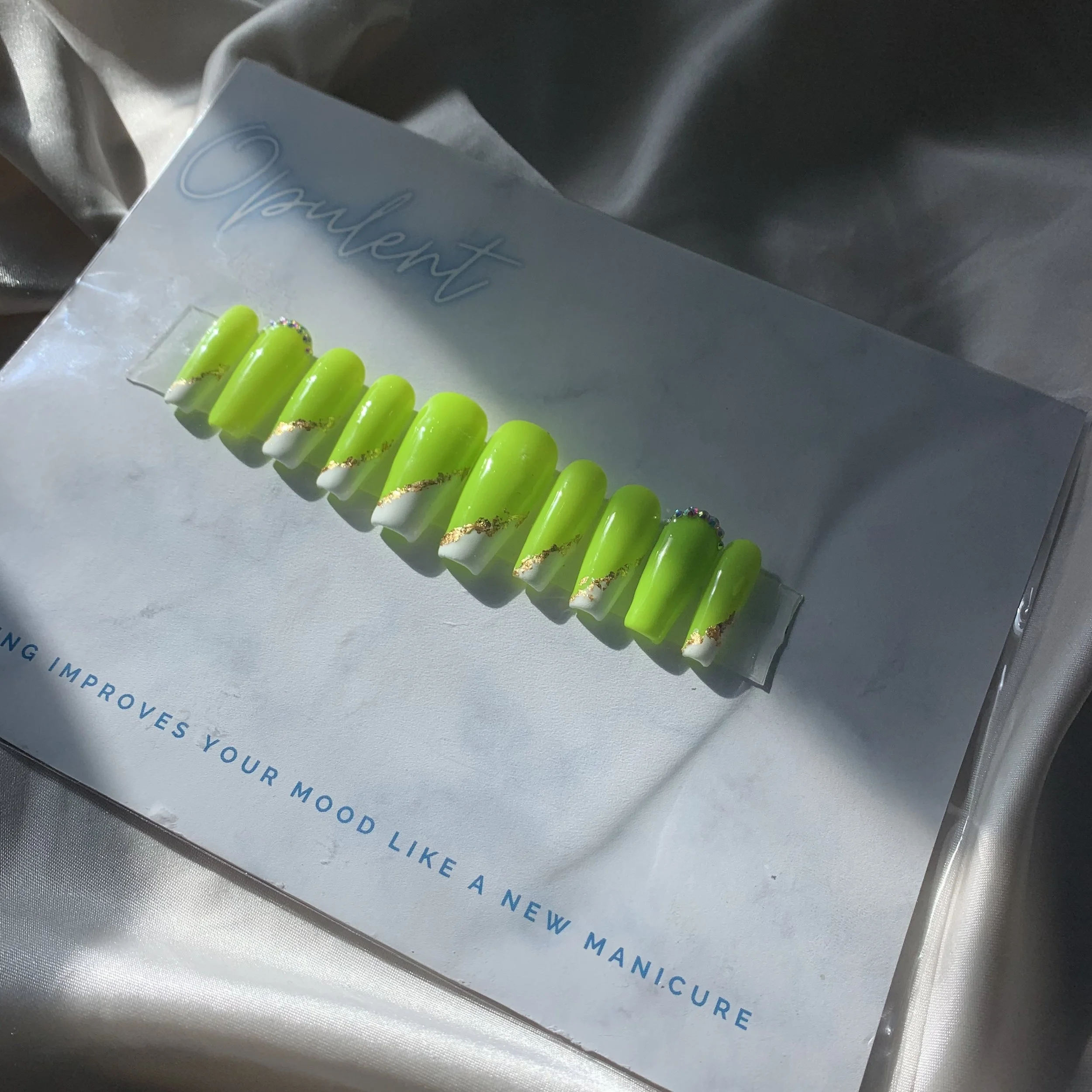 Close-up of a neon green press on nail set in coffin shapes with gold accents.