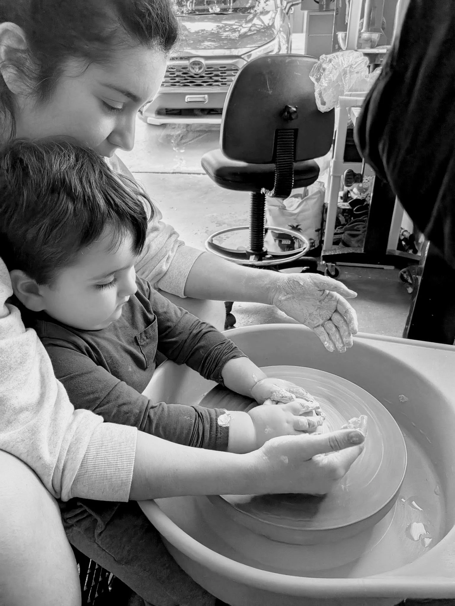 A woman and a child working together at a pottery wheel, shaping wet clay with their hands.