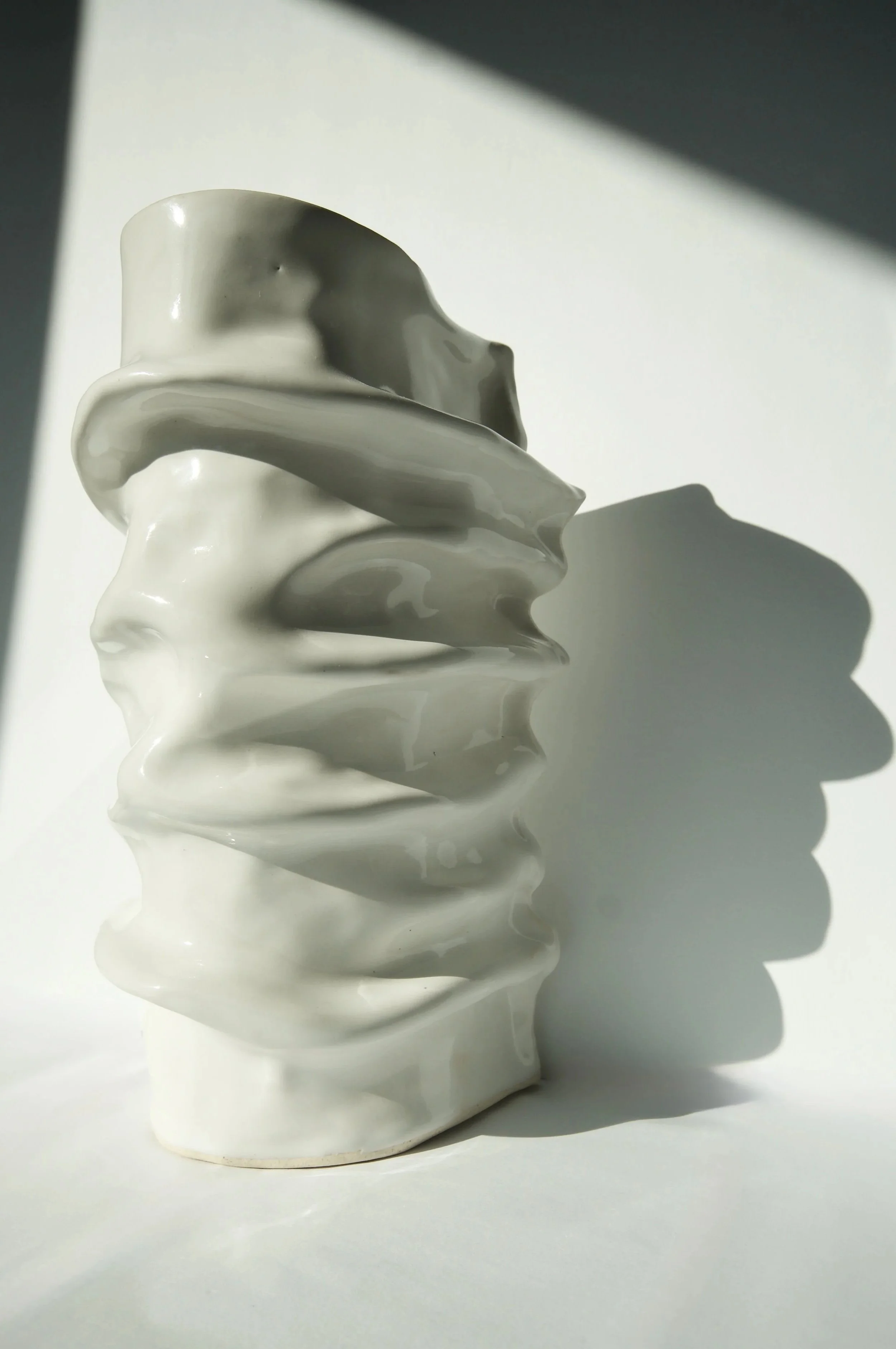 White ceramic sculpture with irregular, wavy layers casting a shadow on a white surface.