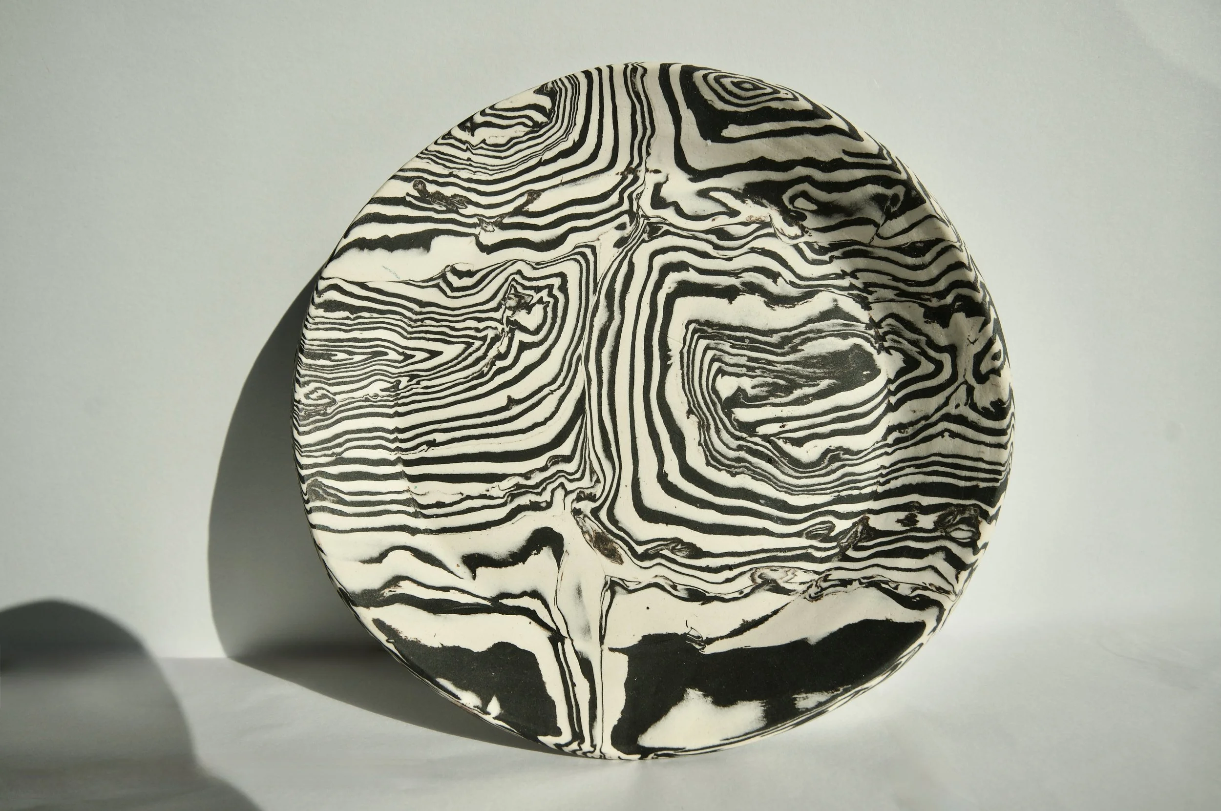 A smooth oval-shaped stone with black and white marbled patterns, casting a shadow on a plain light background.