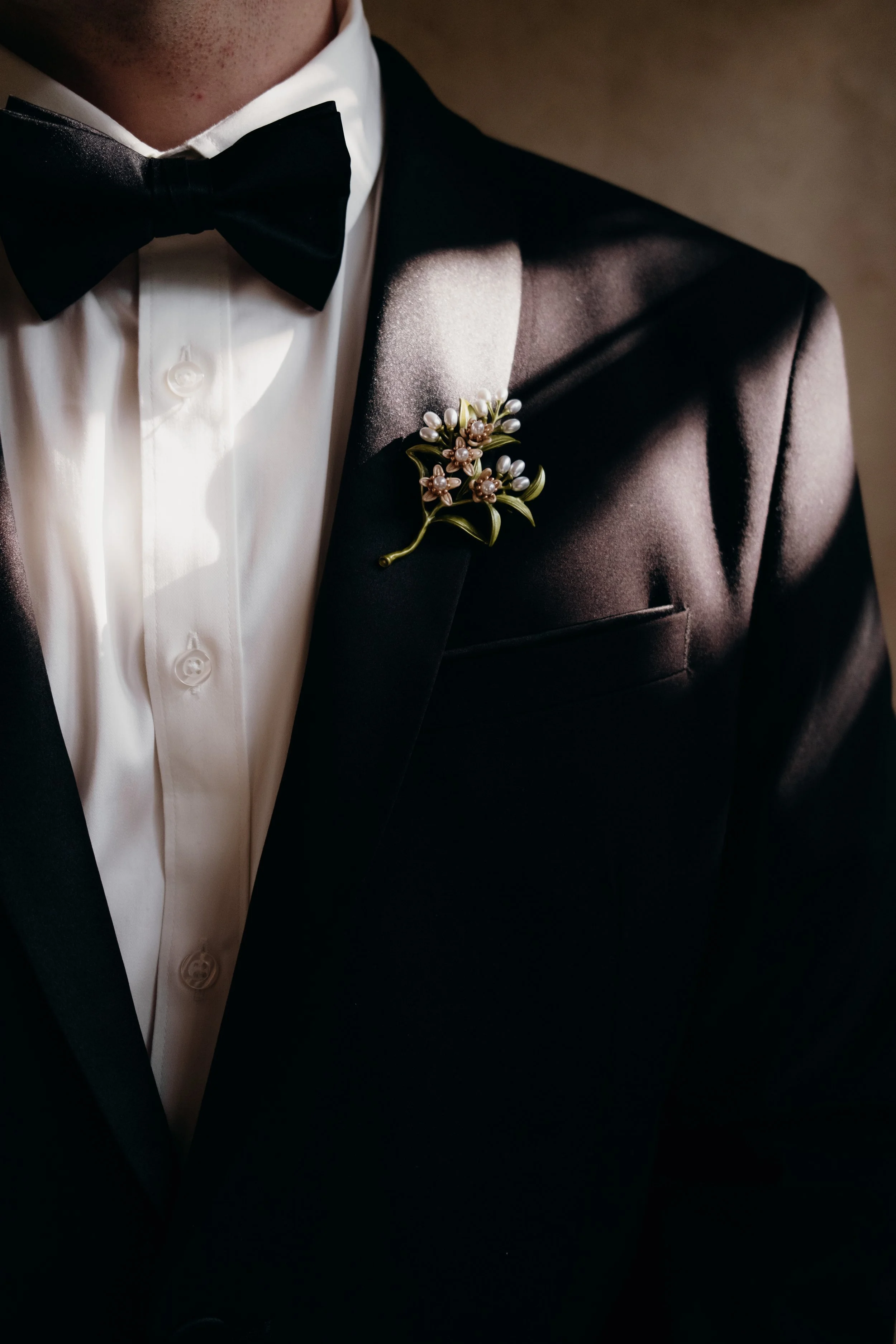 Close-up of a man wearing a tuxedo with a black bow tie, white shirt, and a floral lapel pin.
