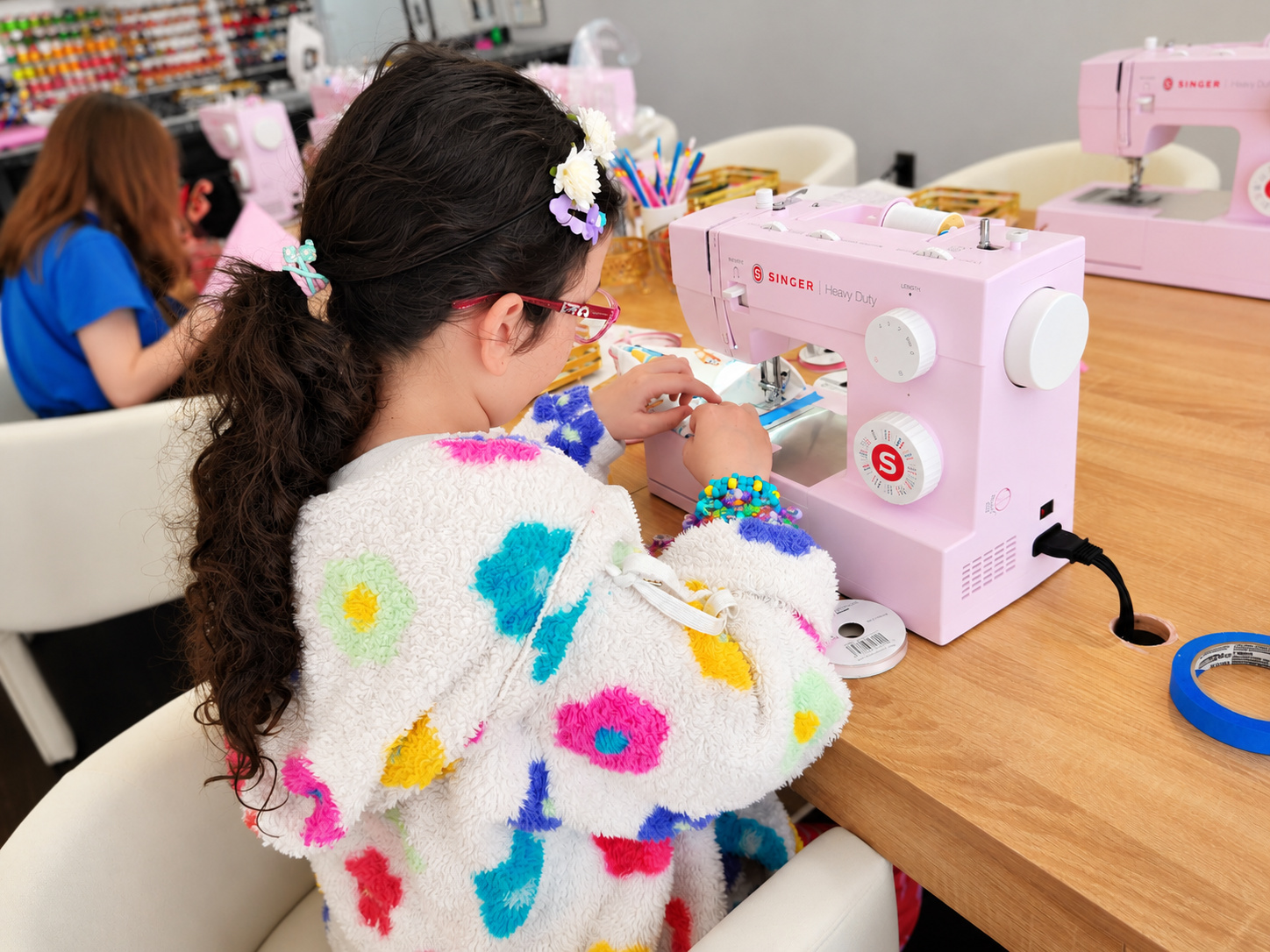 Kids sew drawstring bags on a pink Singer sewing machine.