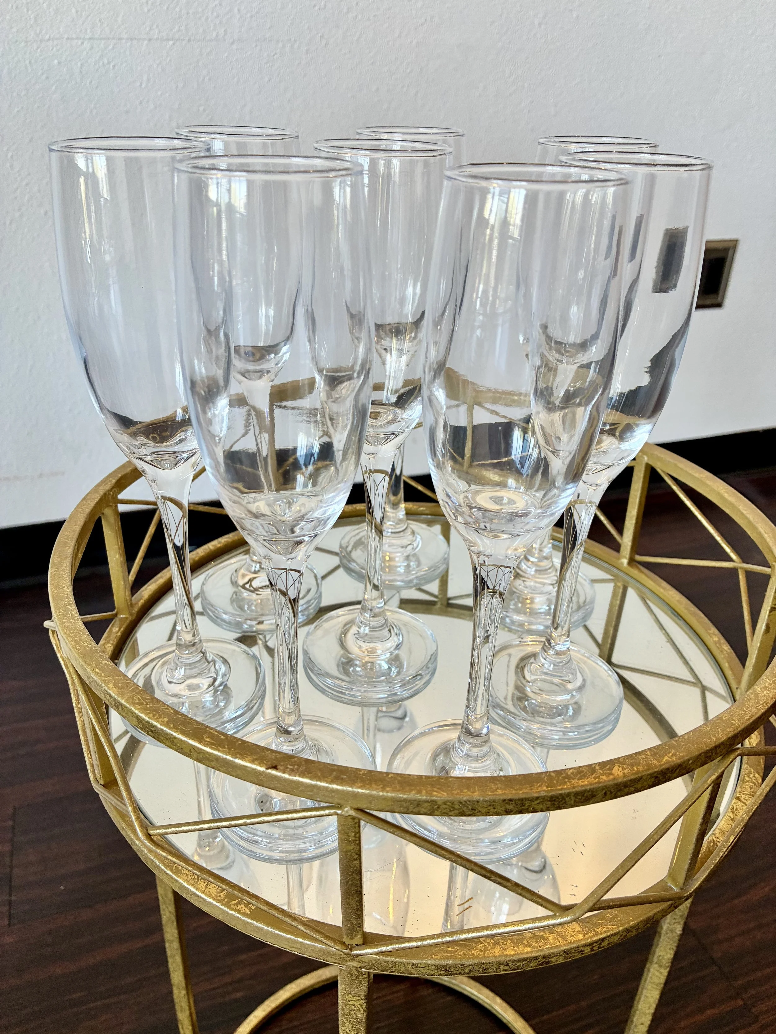 Set of empty champagne flutes on a gold tray, placed on a white mirrored table.