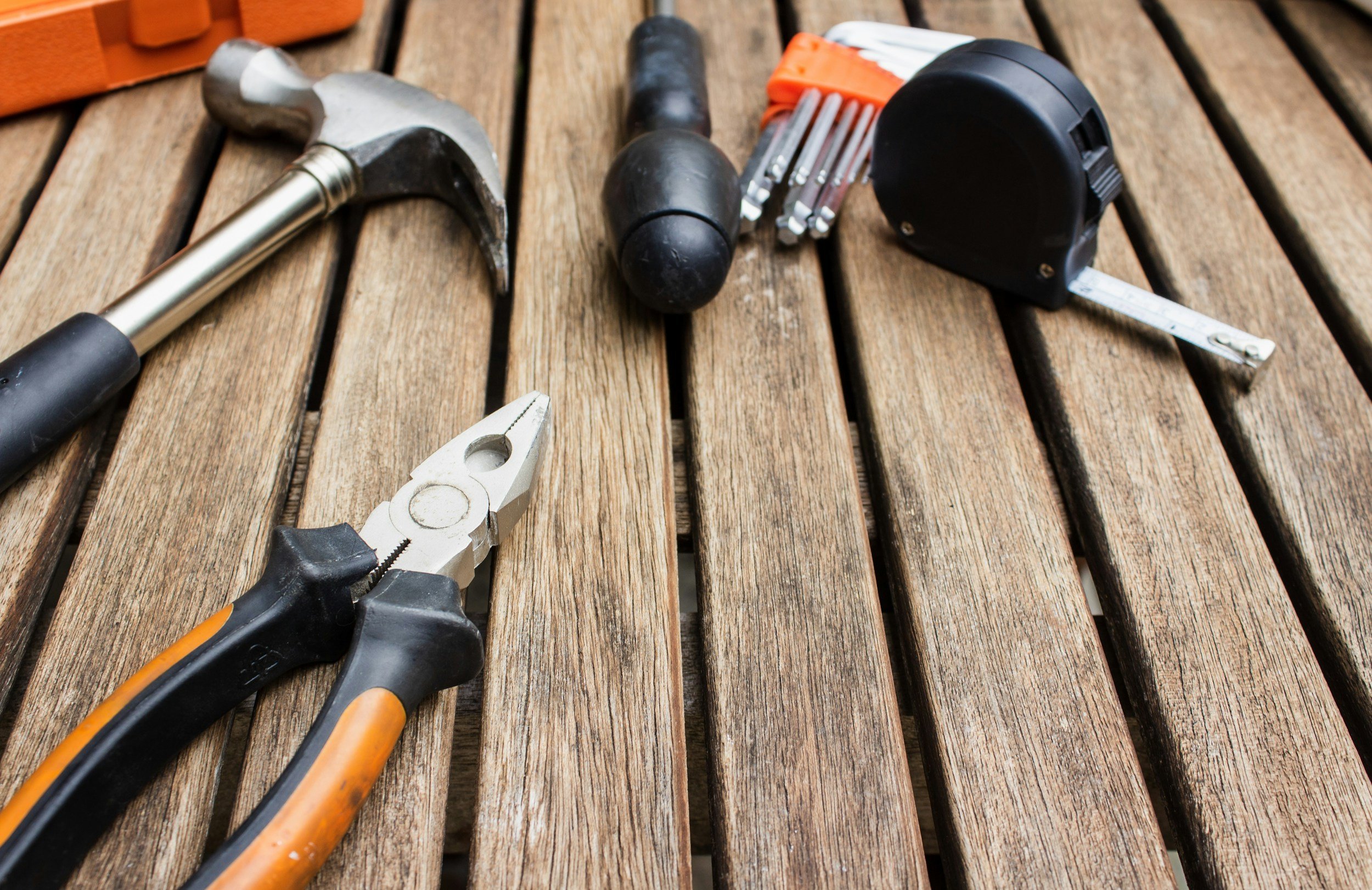 A hammer, screwdriver, pliers, tape measure, and a pack of screws placed on a wooden surface.