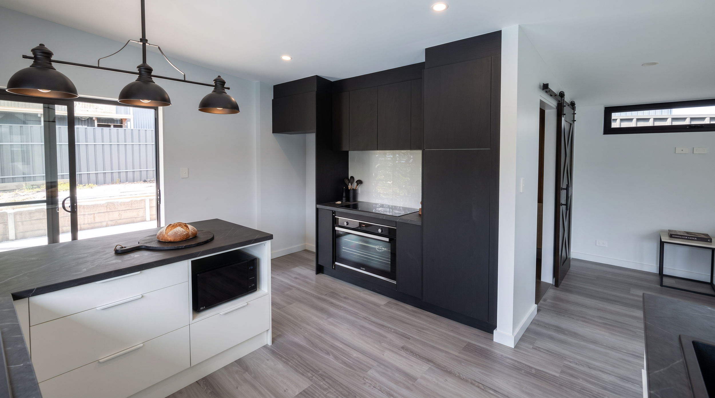 Modern kitchen with black cabinetry, white and gray countertops, a sliding glass door leading outside, and a black industrial-style pendant light fixture.