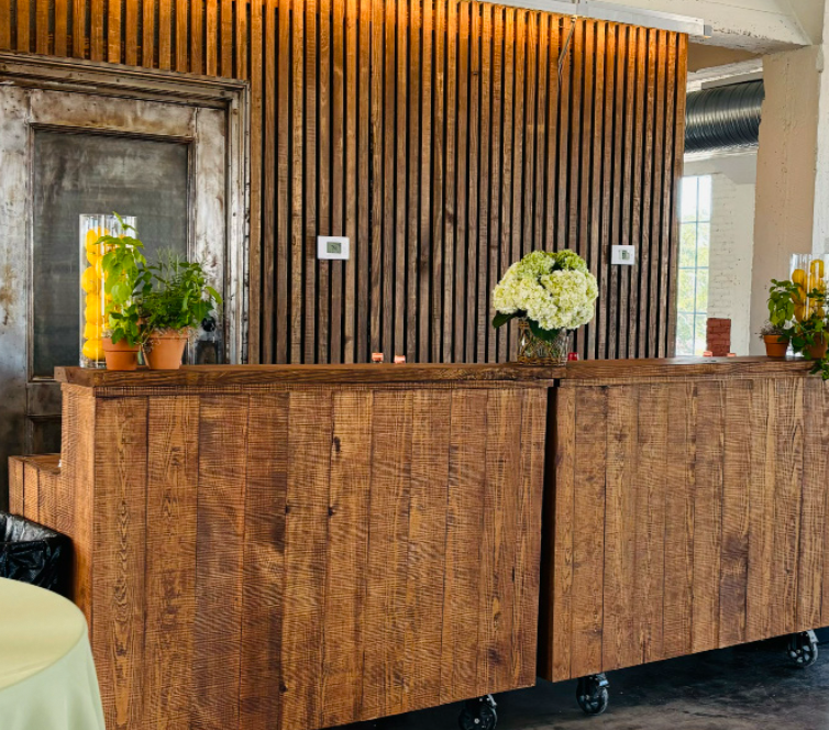 Wooden bar counter with potted plants and a flower arrangement in a modern interior space.
