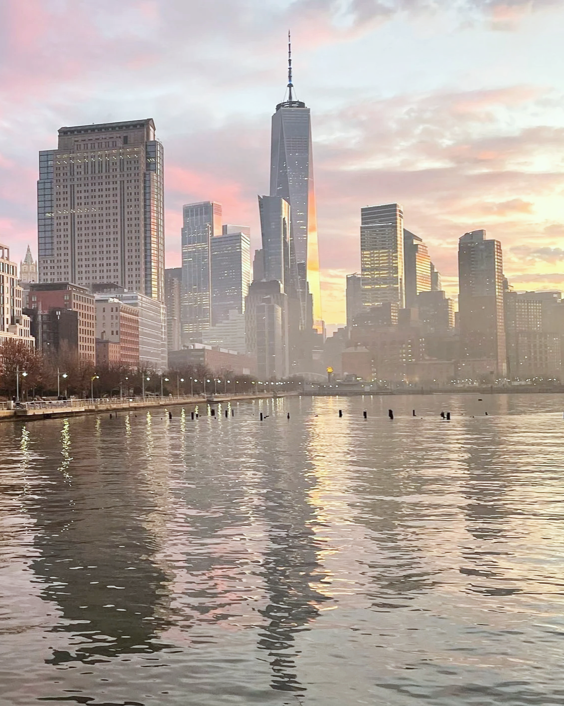 City skyline of Manhattan, New York City with the One World Trade Center building, during sunset, reflected in the river