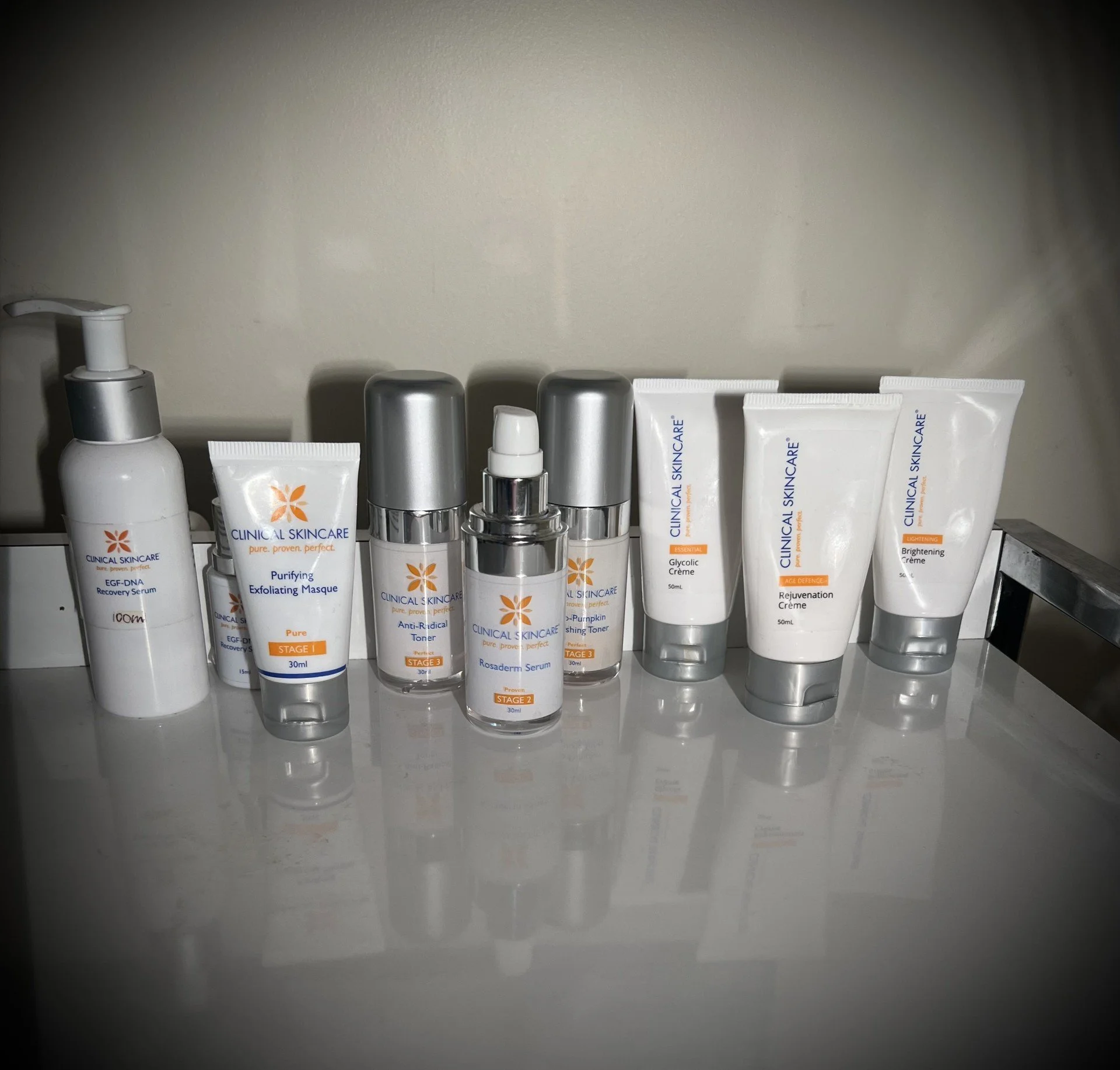 A collection of skincare products, including tubes and bottles, arranged on a white shelf against a plain beige wall.