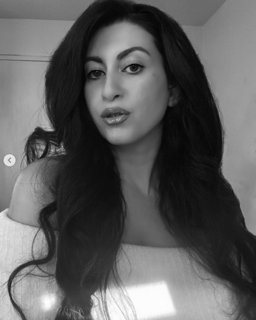 Black and white photo of a woman with long wavy hair looking at the camera, with one shoulder slightly exposed.