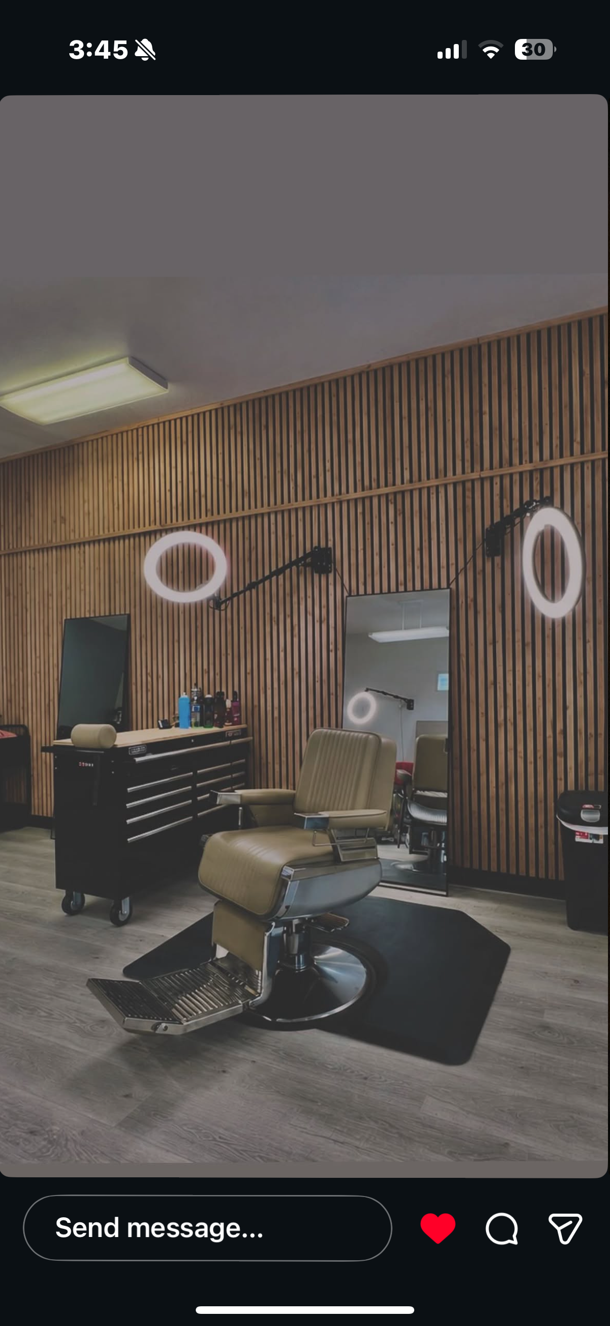 Inside a modern barbershop with a vintage barber chair, wooden wall paneling, round LED mirror lights, a black tool chest, and mirrors reflecting part of the room.