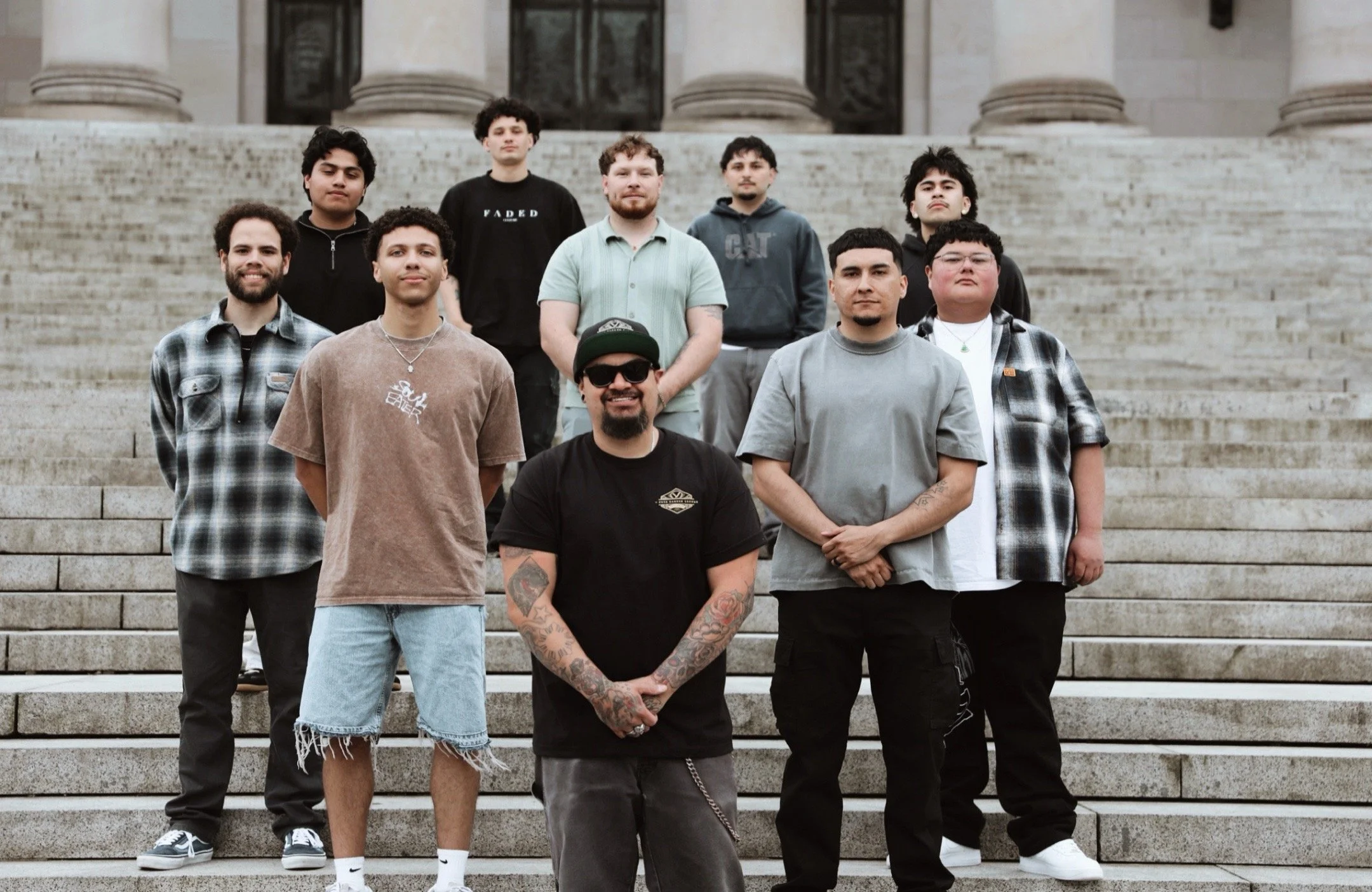 A group of ten young men standing on stone steps in front of a building with large columns.