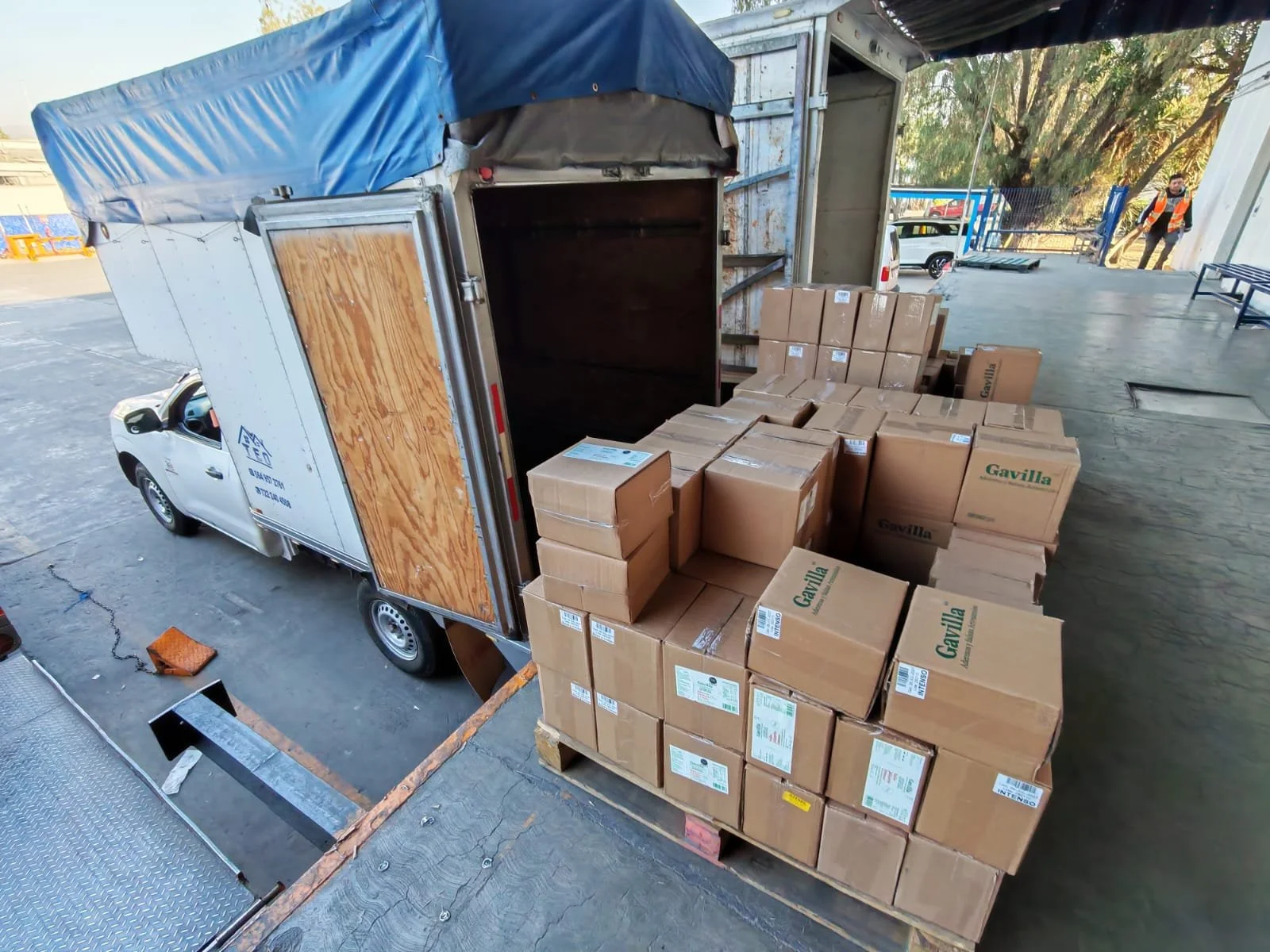Camioneta de carga con caja abierta y varias cajas de cartón apiladas lista para ser descargada en un almacén