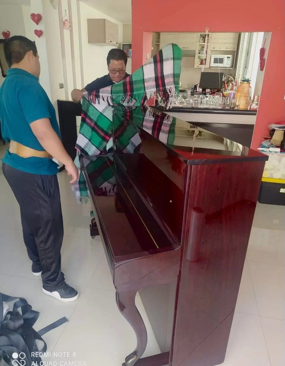 Dos personas colocando una manta sobre un piano de madera para protegerlo y evitar daños