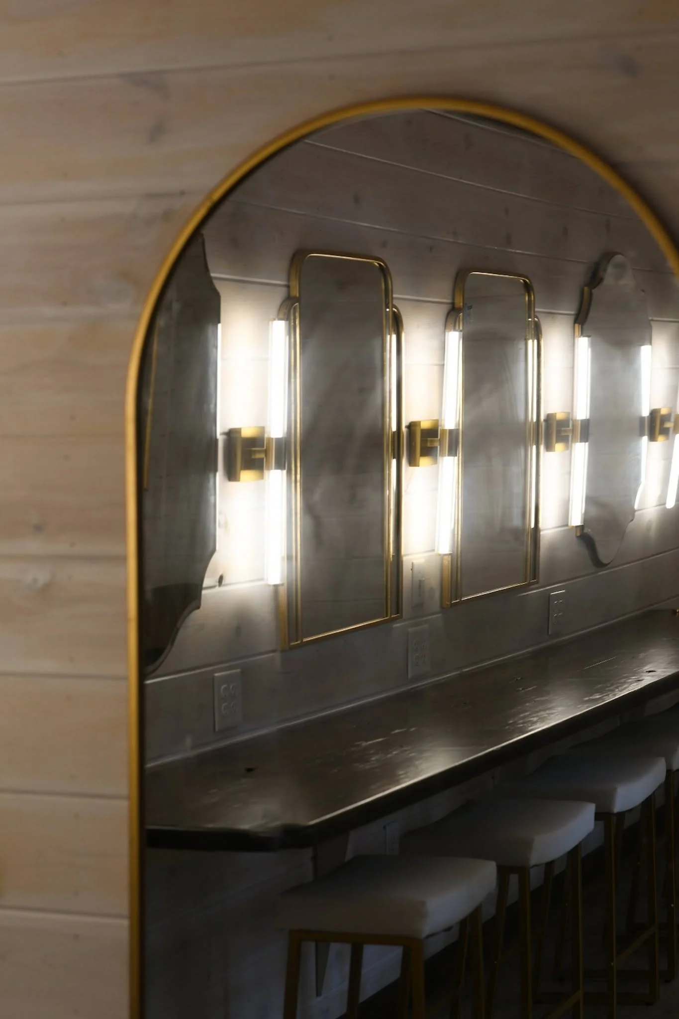 A modern dressing area with a wooden counter, illuminated by vertical light fixtures, and beige stools underneath, in an interior setting.