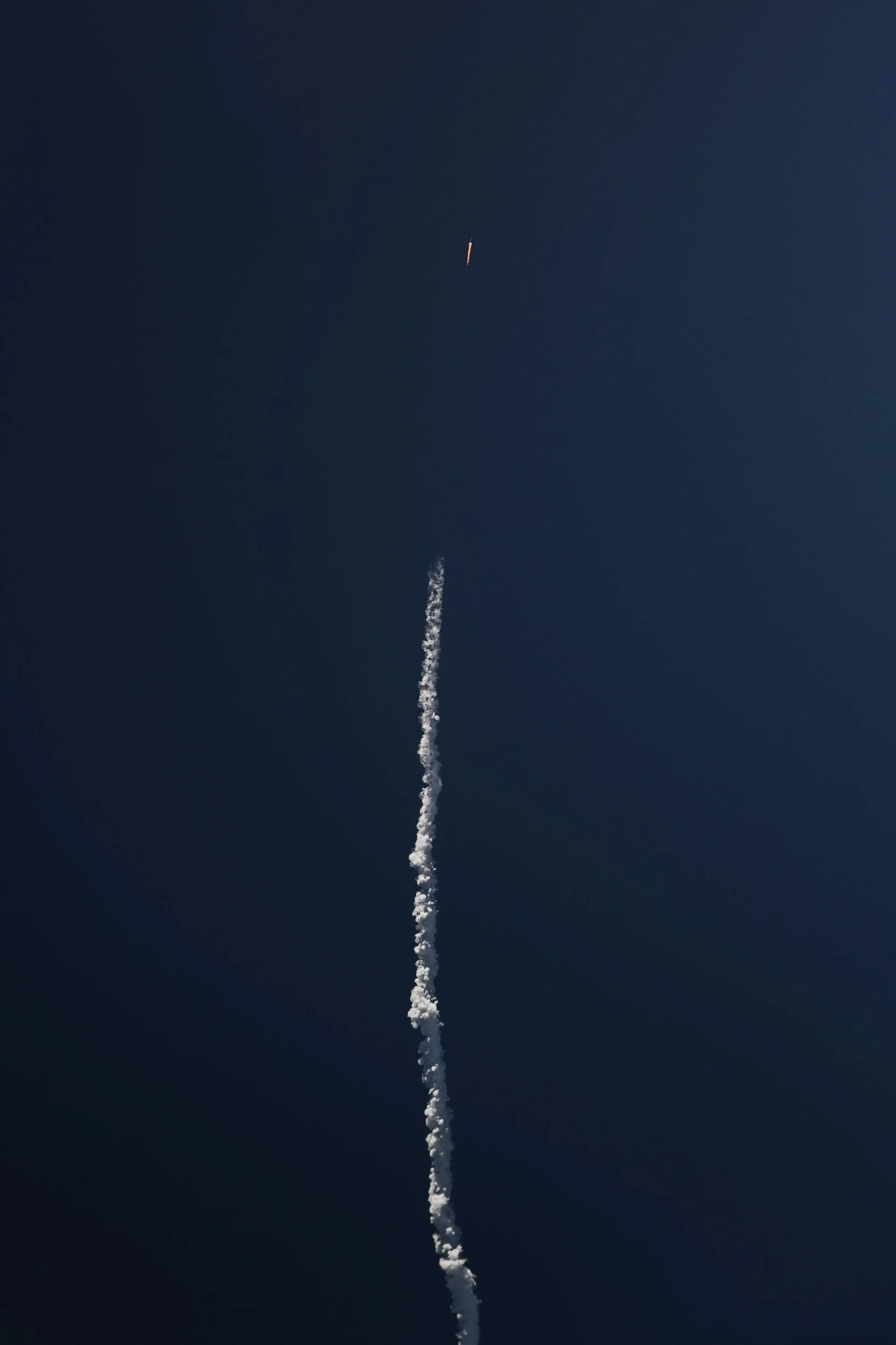 A daytime photo of a rocket launching into the sky with a trail of white smoke below it.