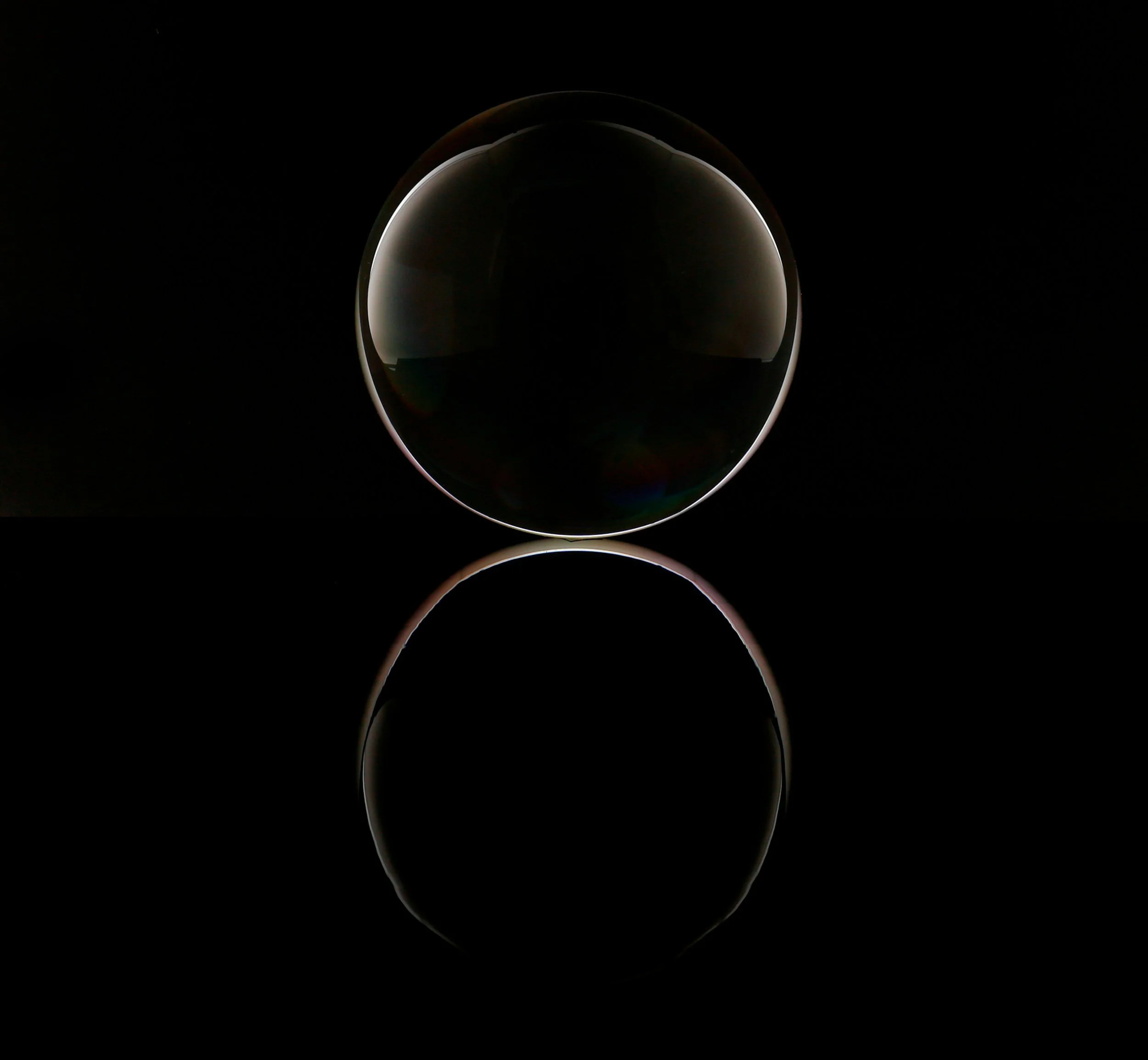 Close-up of a transparent sphere with a reflective surface, set against a black background, creating a glowing effect along its edge.