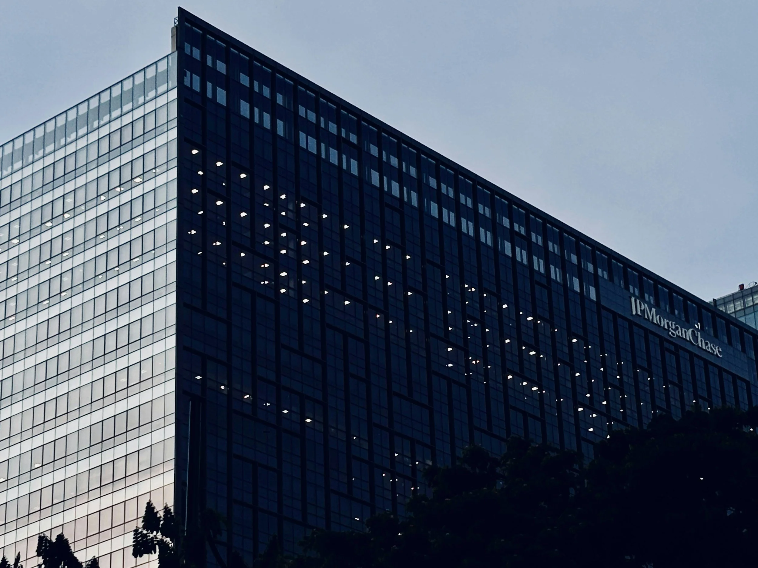 A tall modern glass office building with illuminated windows at dusk or night, with the 'JPMorgan Chase' logo on the side.
