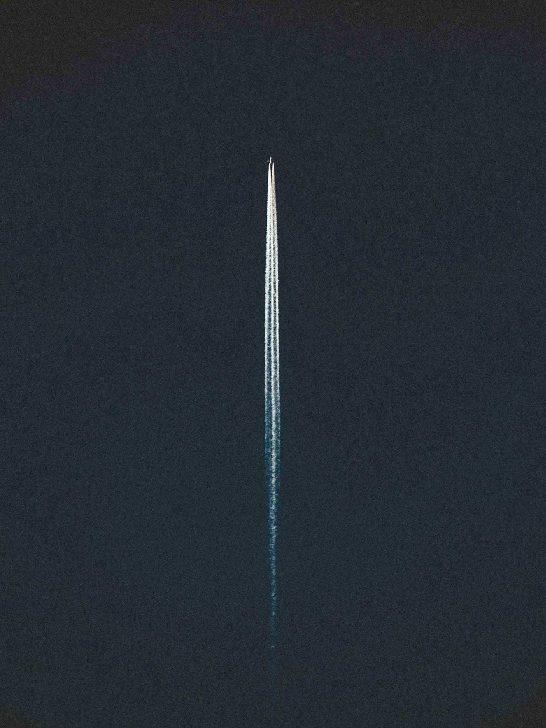 A person parachuting at night, descending with a trail of white parachute cords visible against the dark sky.