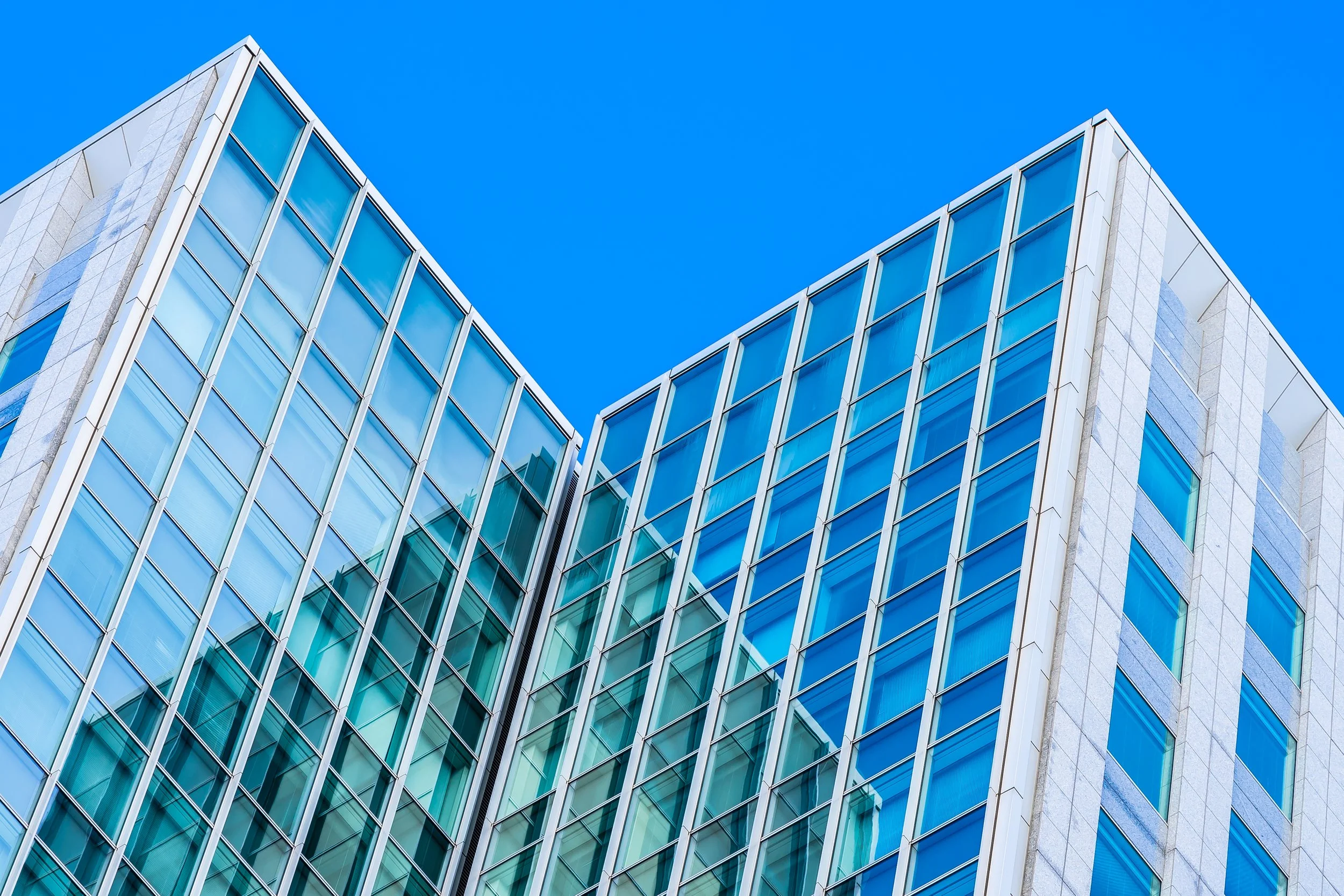 Modern glass office building with reflective windows against a clear blue sky.
