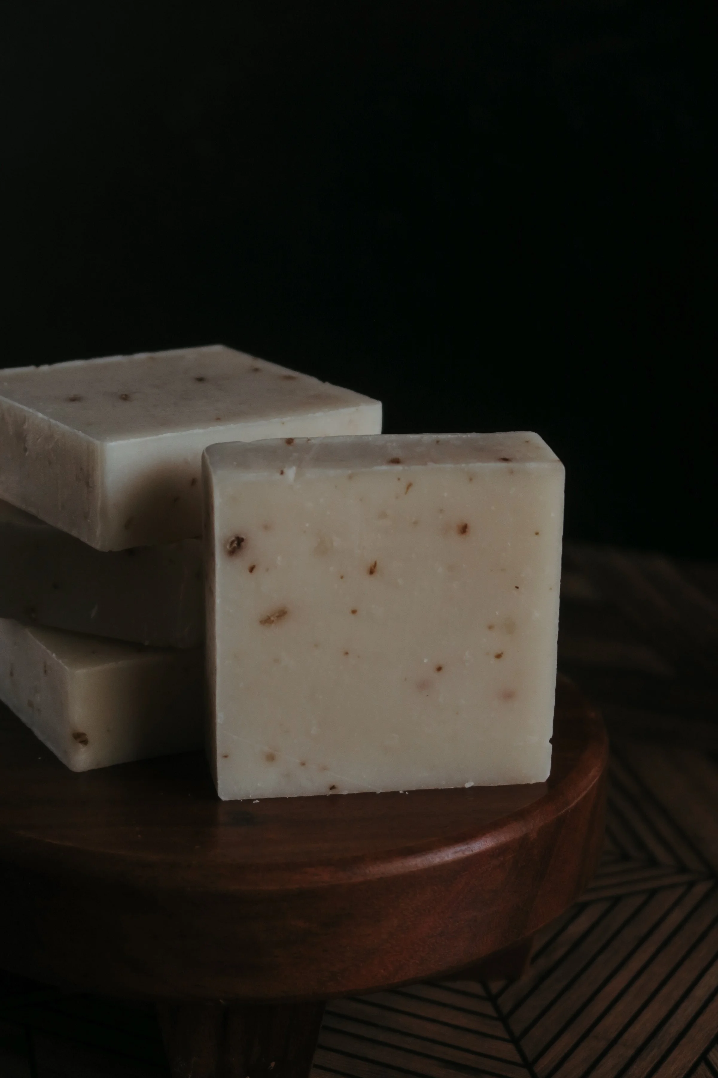 Close-up of a stack of white soap bars with small brown specks, placed on a round wooden tray.