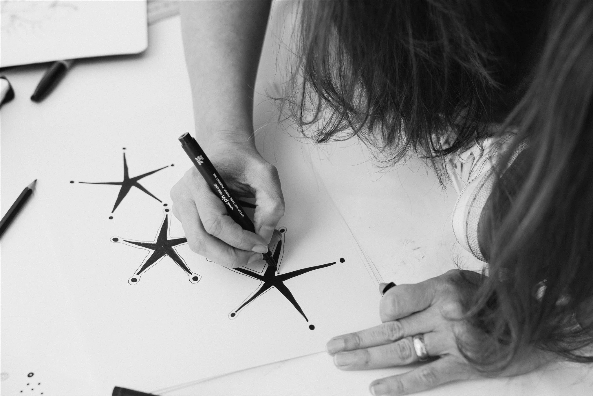 Kate drawing stars on paper with black marker in black and white photograph.