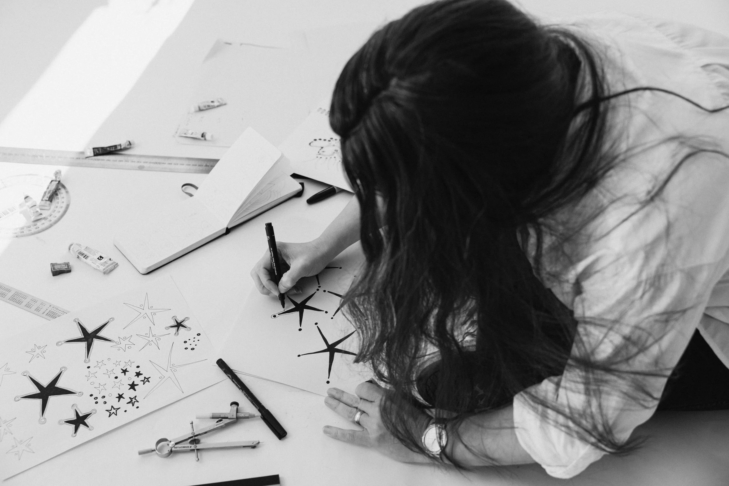 Kate drawing star shapes on a paper on the ground, surrounded by drawing tools and sketches.