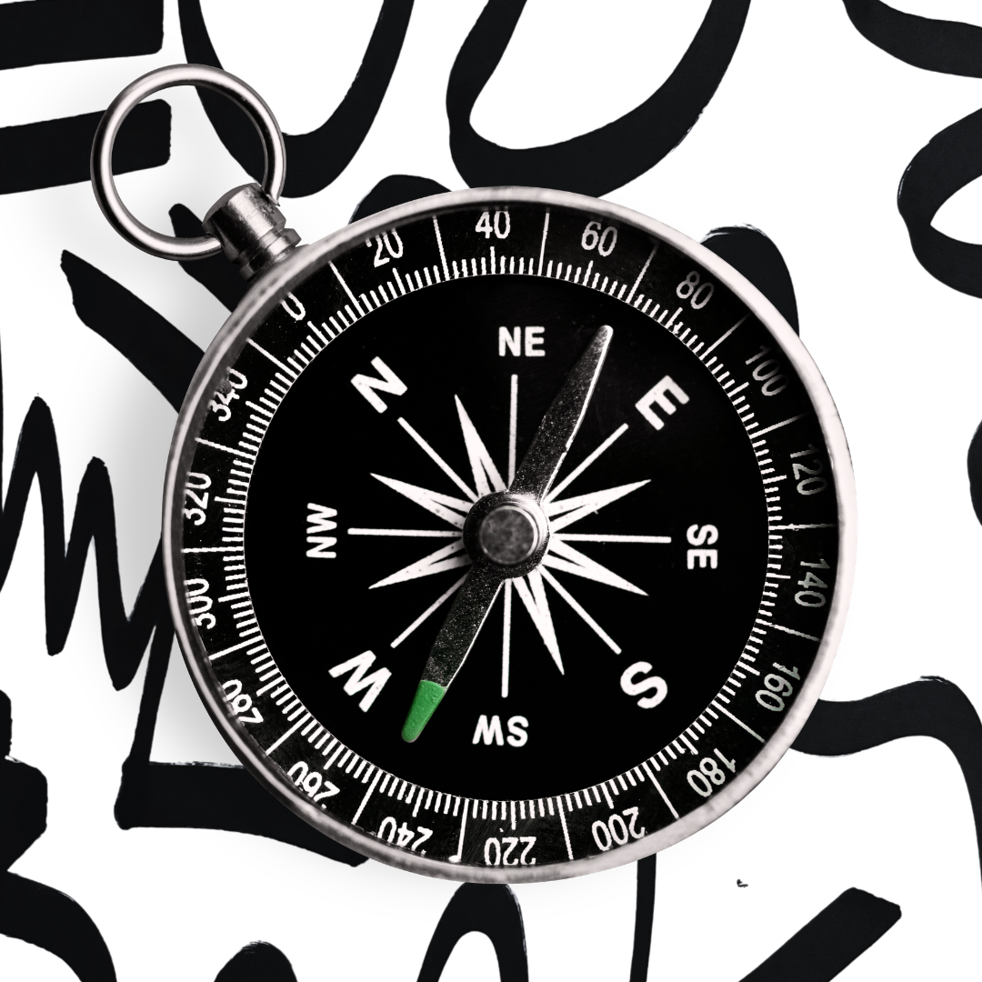 A silver compass with a black face, placed on a black and white patterned surface.