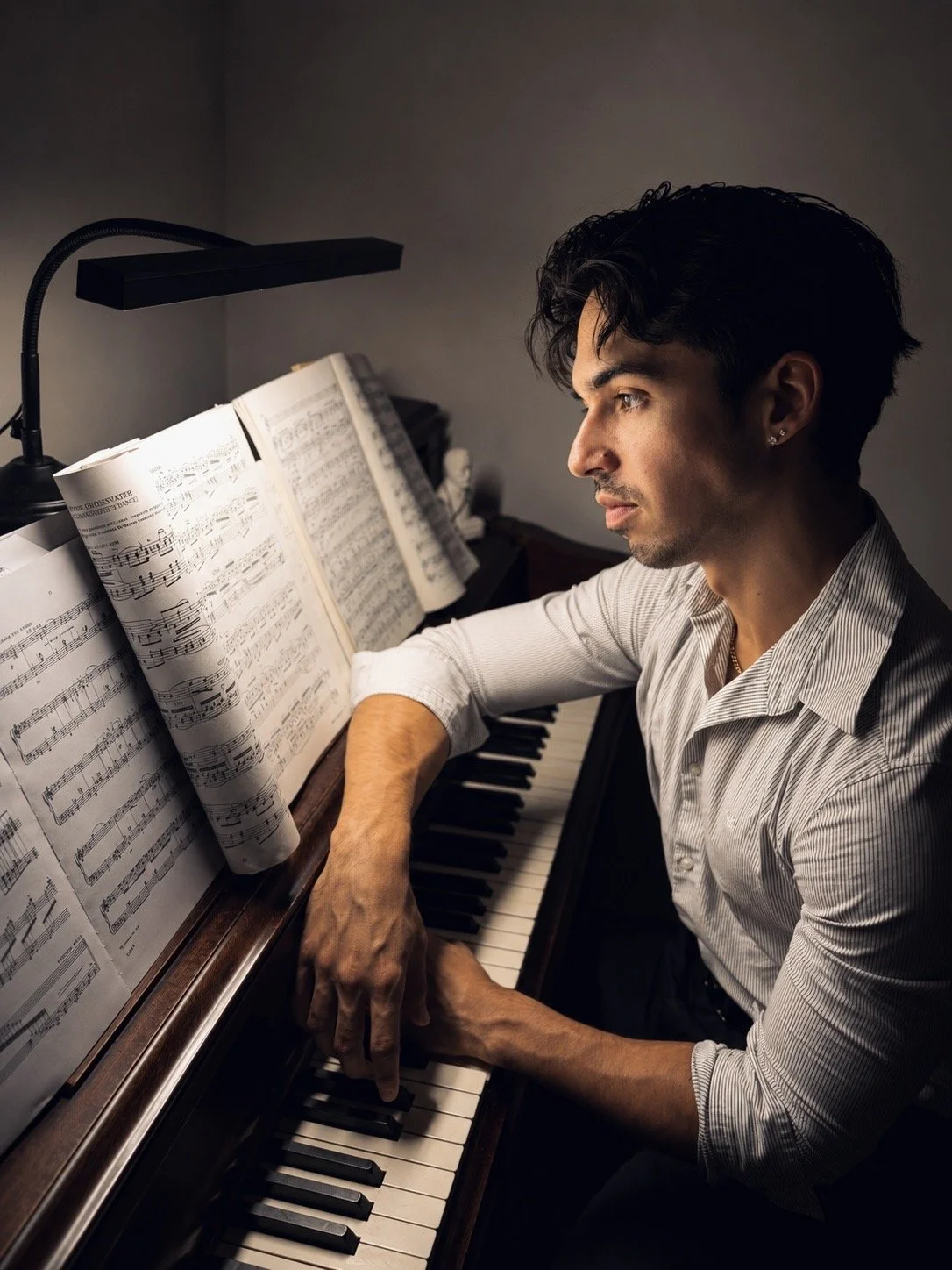 A man playing the piano in a dimly lit room with sheet music on the music stand.