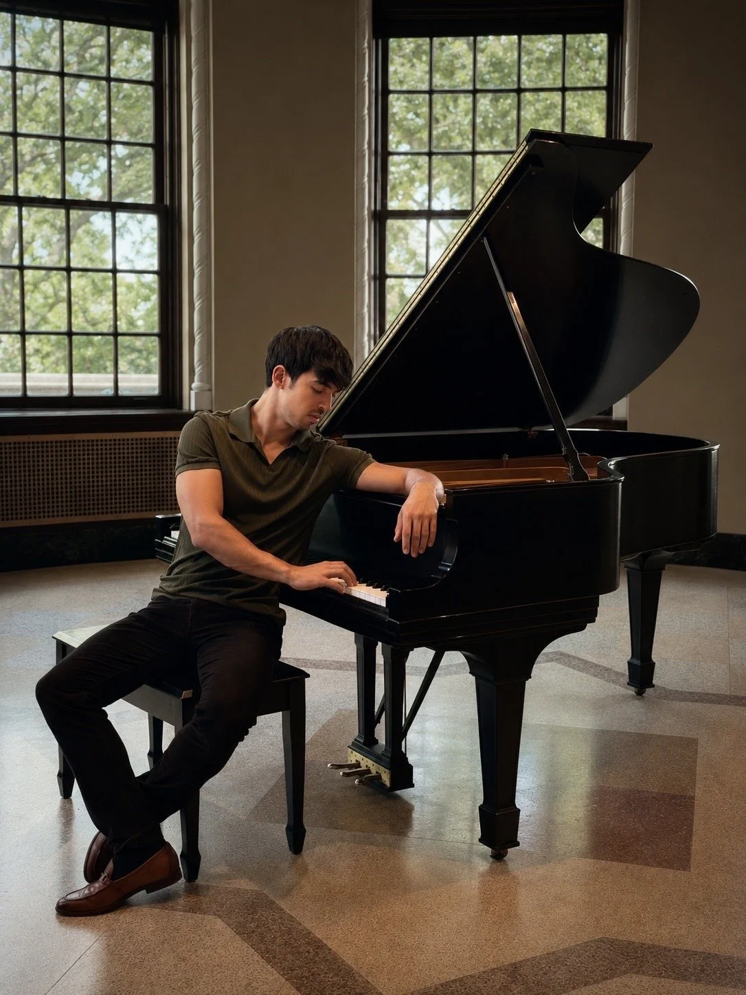 A man playing a grand piano in a room with large windows.