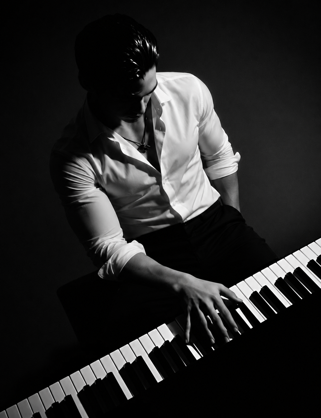Black and white photo of a man in a white shirt playing a piano, with dark background and dramatic lighting.