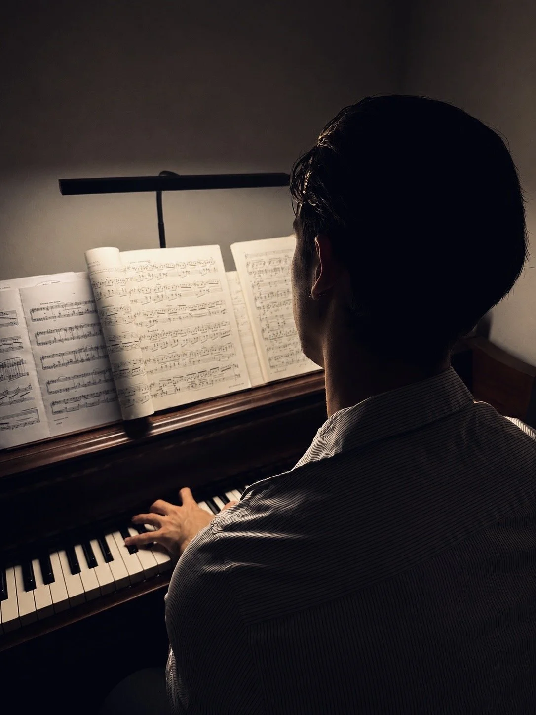 Man playing piano in dim lighting, facing sheet music on music stand