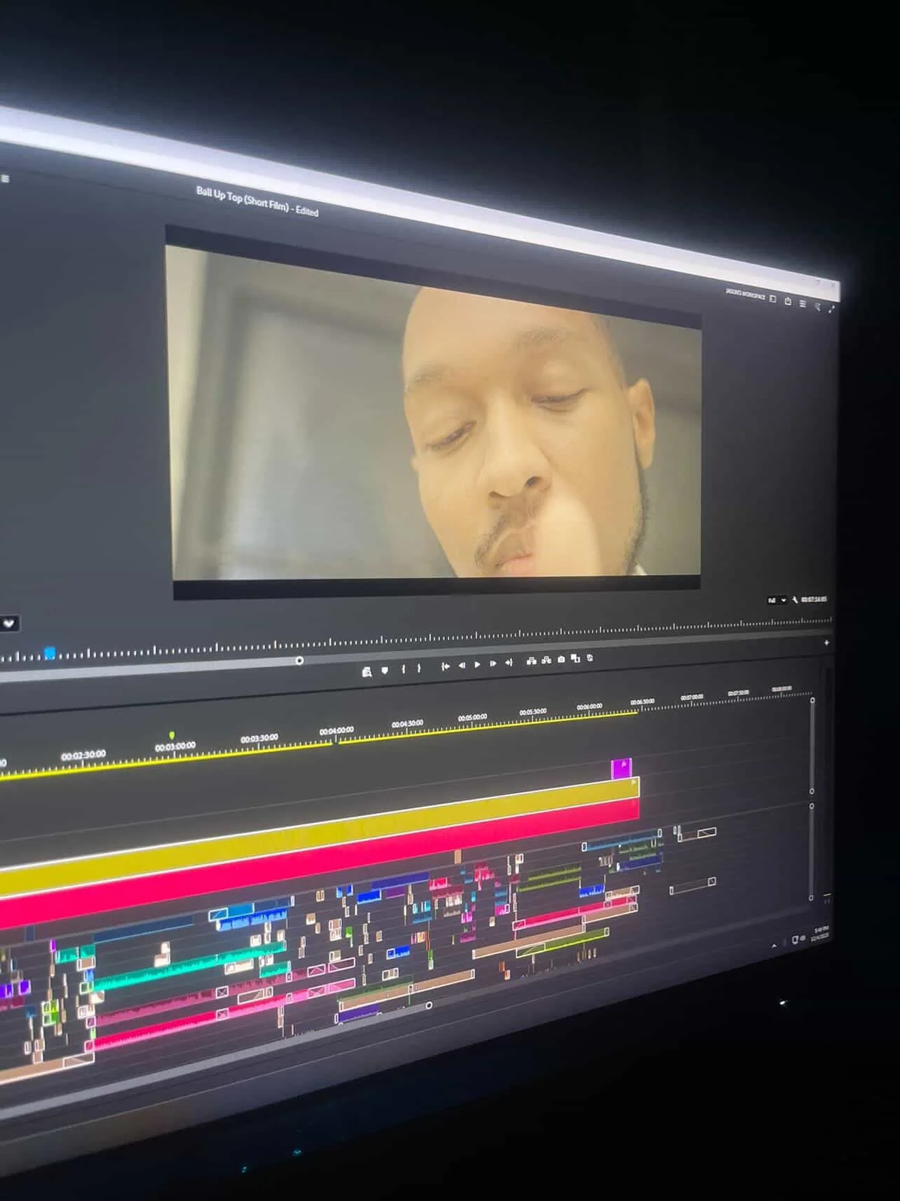 Computer screen displaying a video editing timeline with colorful clips and a still from a movie or TV show featuring a person's face with closed eyes.