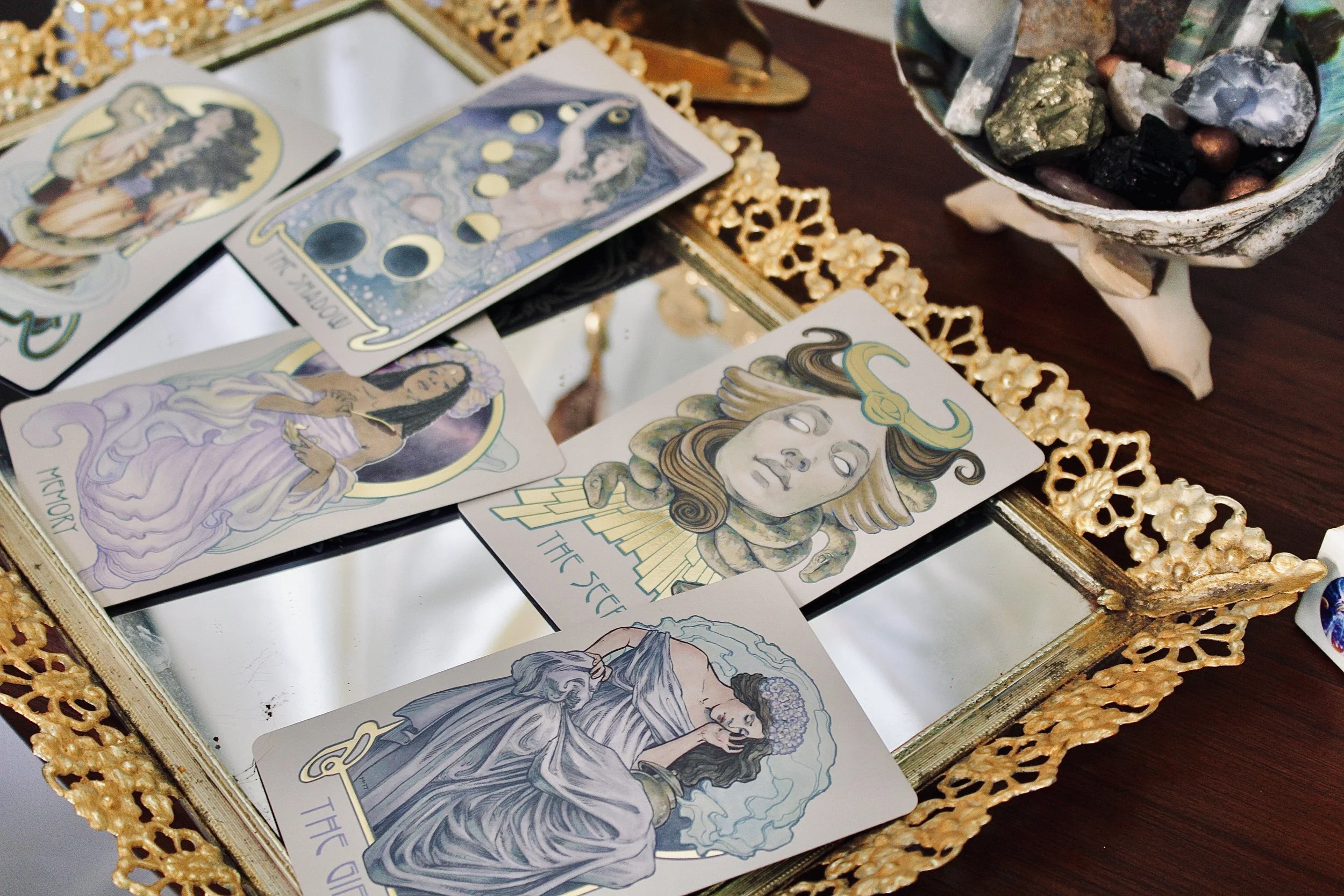 Tarot cards spread out on a surface, with an ornate gold framing and a bowl of assorted stones nearby.