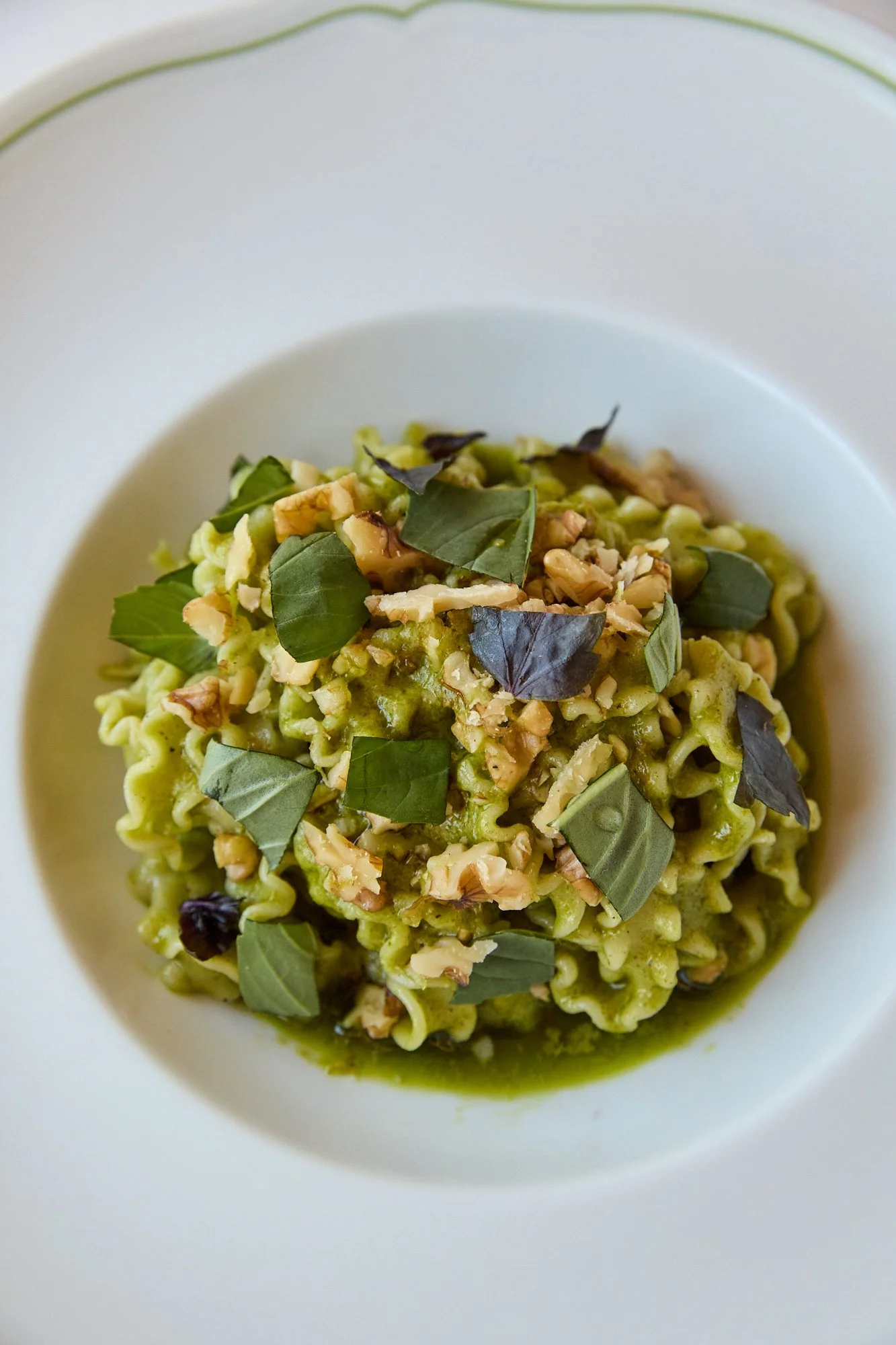 Close-up of a pasta dish bowl filled with noodles topped with crushed walnuts and fresh basil leaves.