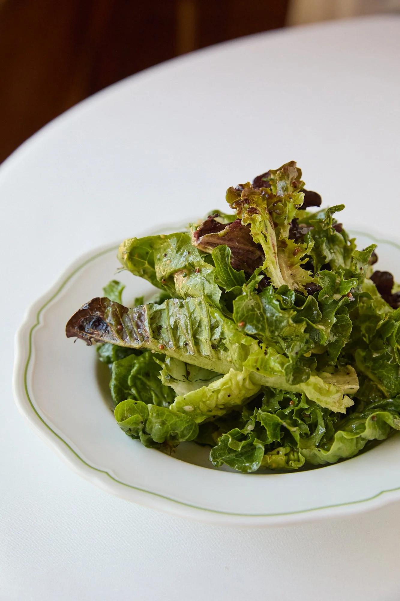 A plate of mixed green salad with leafy lettuce on a white dish with gold trim.