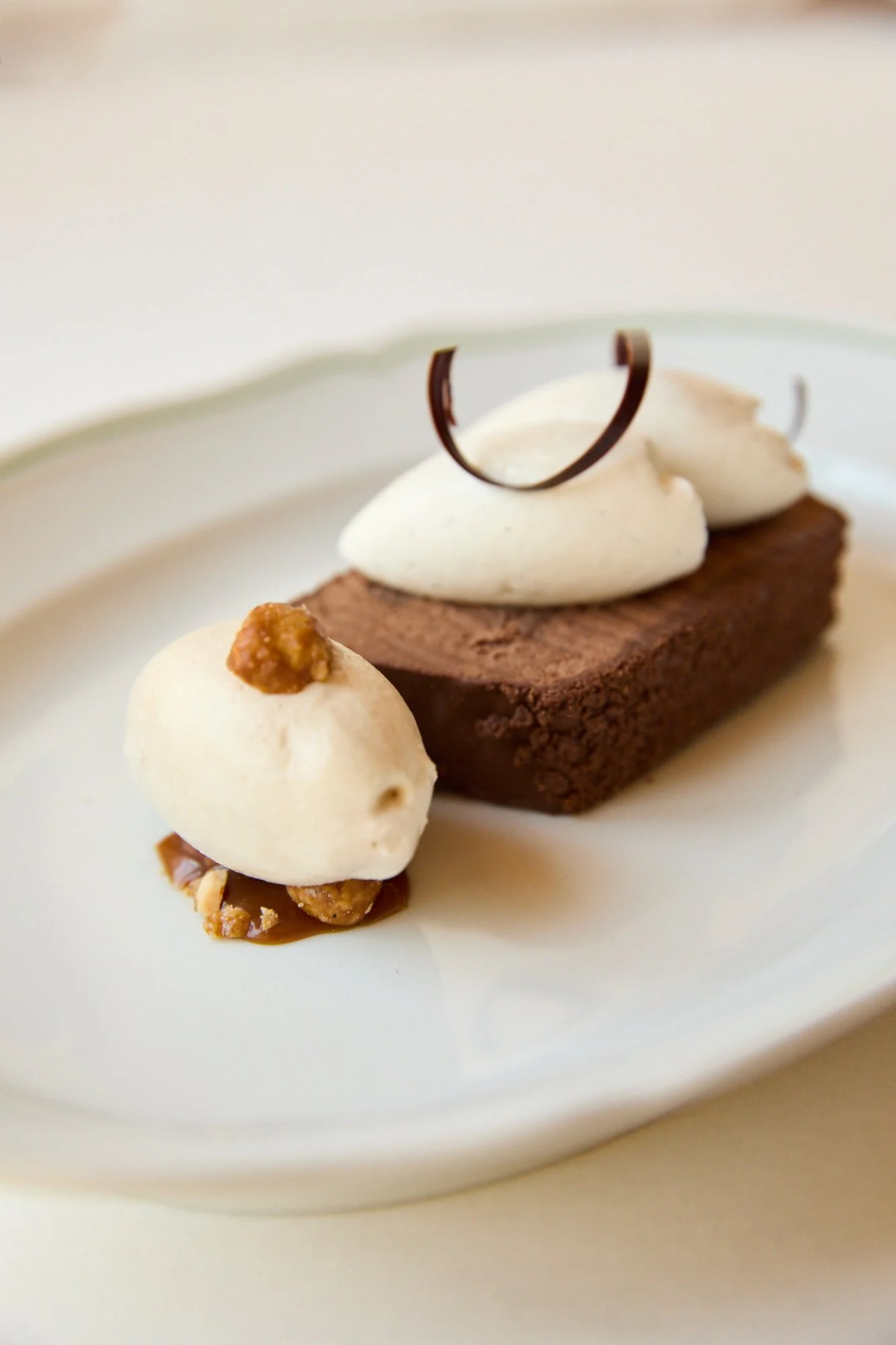 A close-up photo of a chocolate mousse dessert topped with, whipped cream, and a decorative chocolate curl on a white plate.