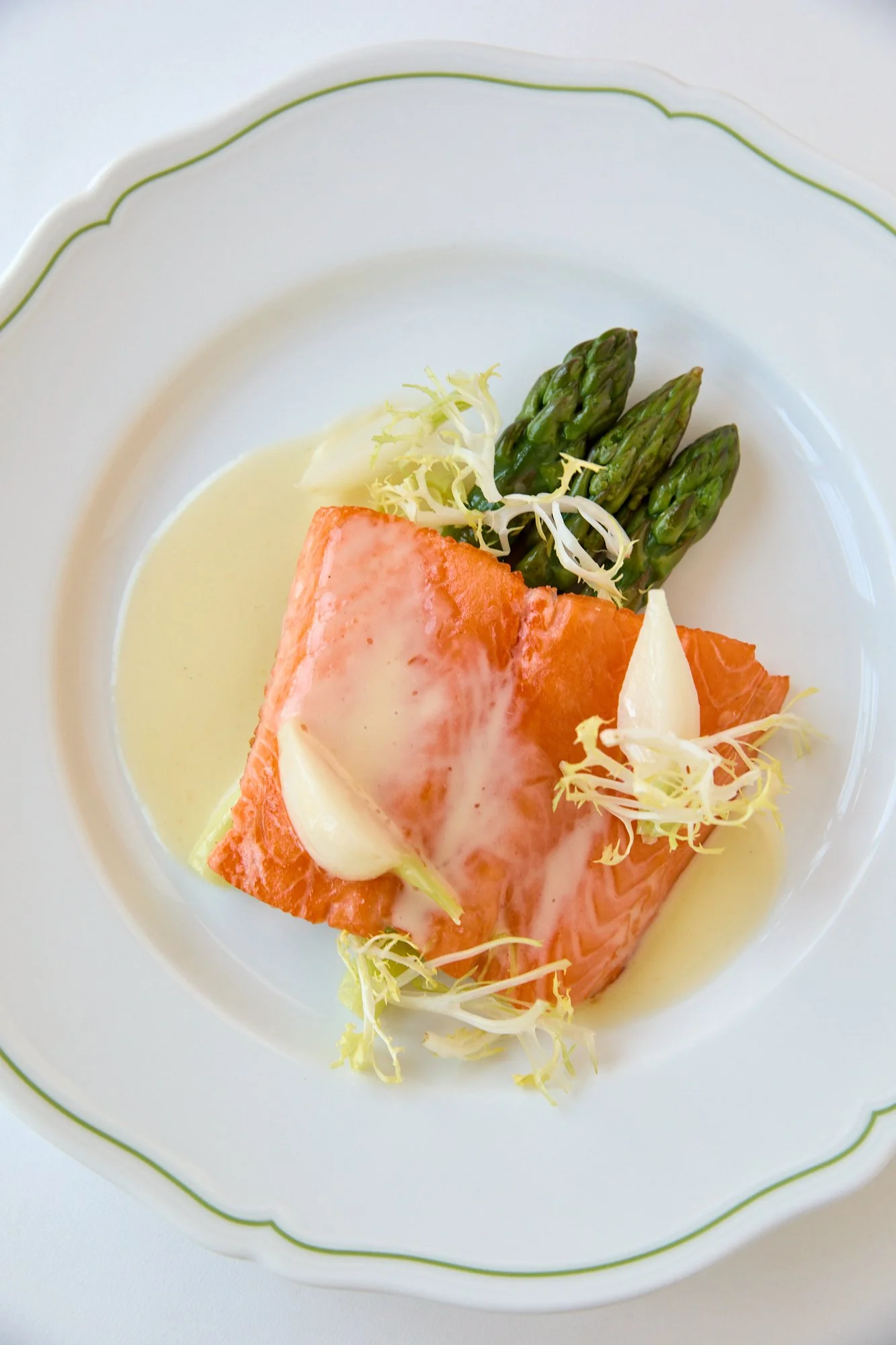 A plate with a piece of cooked salmon, asparagus, and some shredded lettuce, all topped with a creamy white sauce.