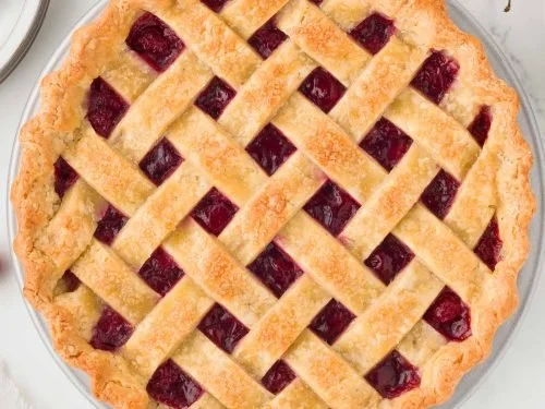 A freshly baked cherry pie with a lattice crust, showing cherry filling underneath.