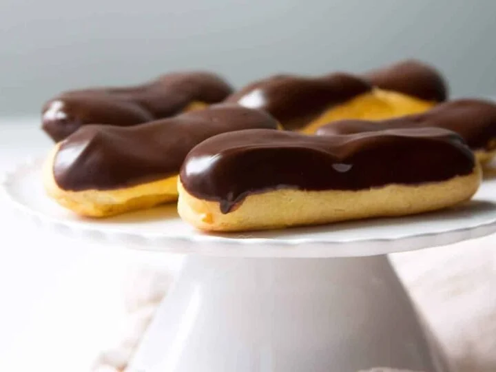 Chocolate éclairs on a white cake stand.