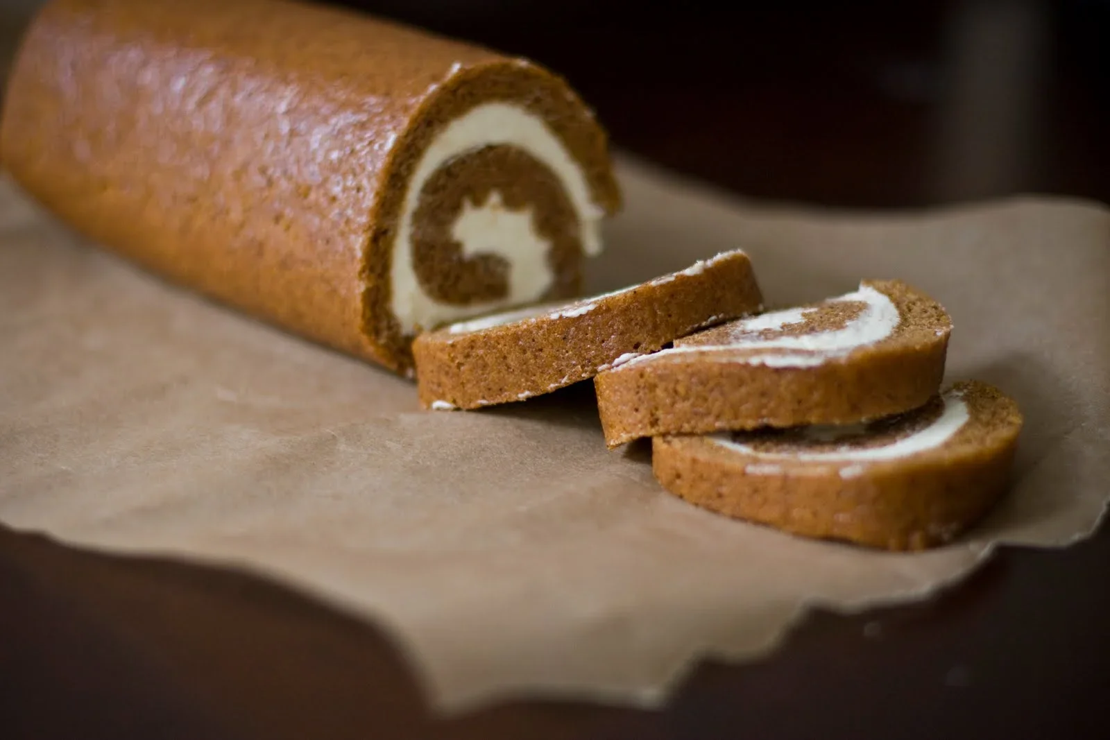 Chocolate roll cake with white filling, partially sliced on parchment paper.