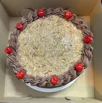 A round cake decorated with purple frosting and red cherries, with a white outer layer, inside a box.