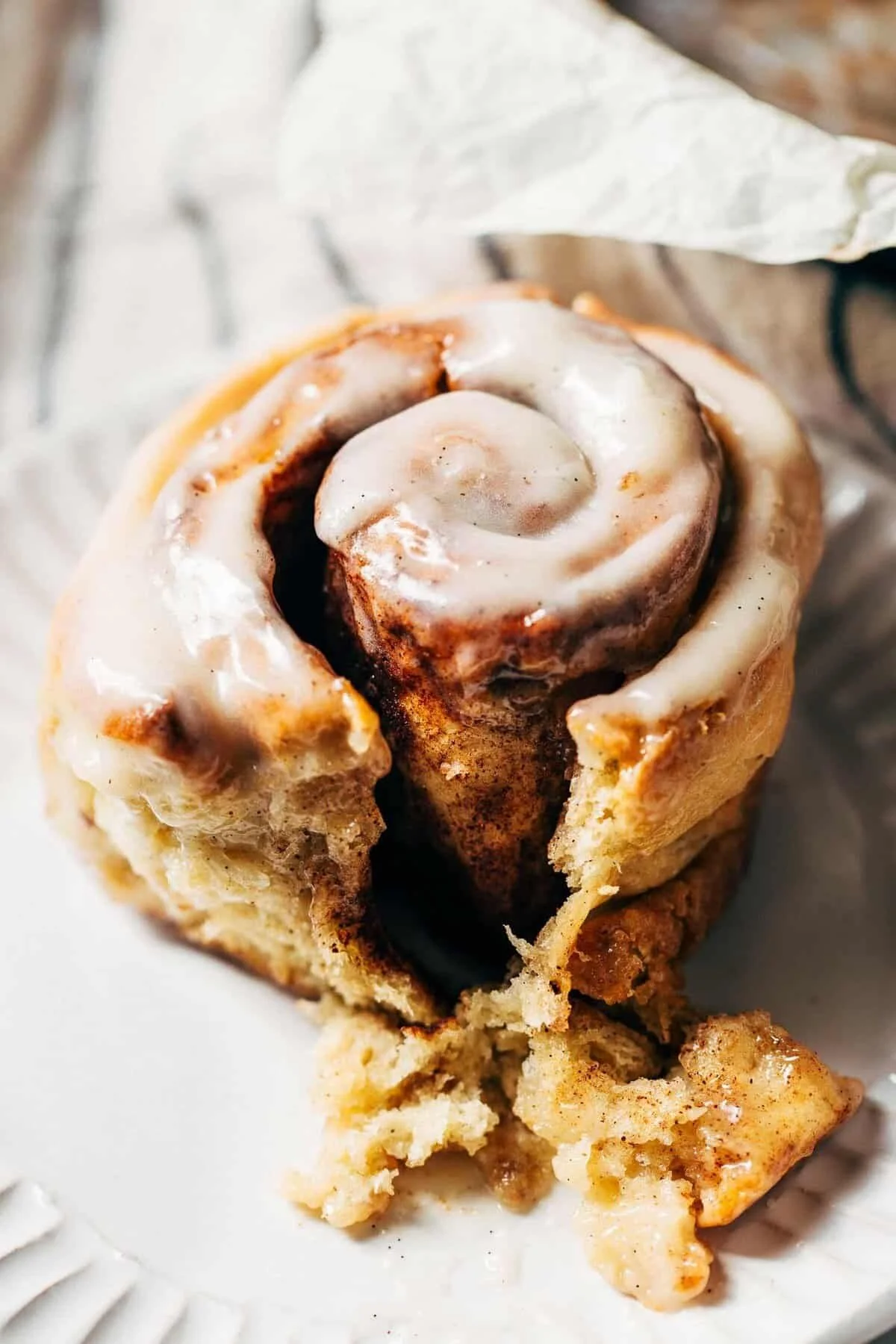 Close-up of a cinnamon roll with icing, partially eaten, on a white plate.
