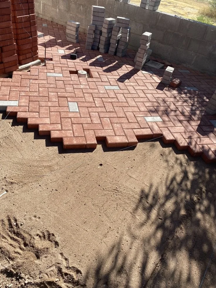Brick pavers being laid on a construction site, with stacked bricks and tools nearby.