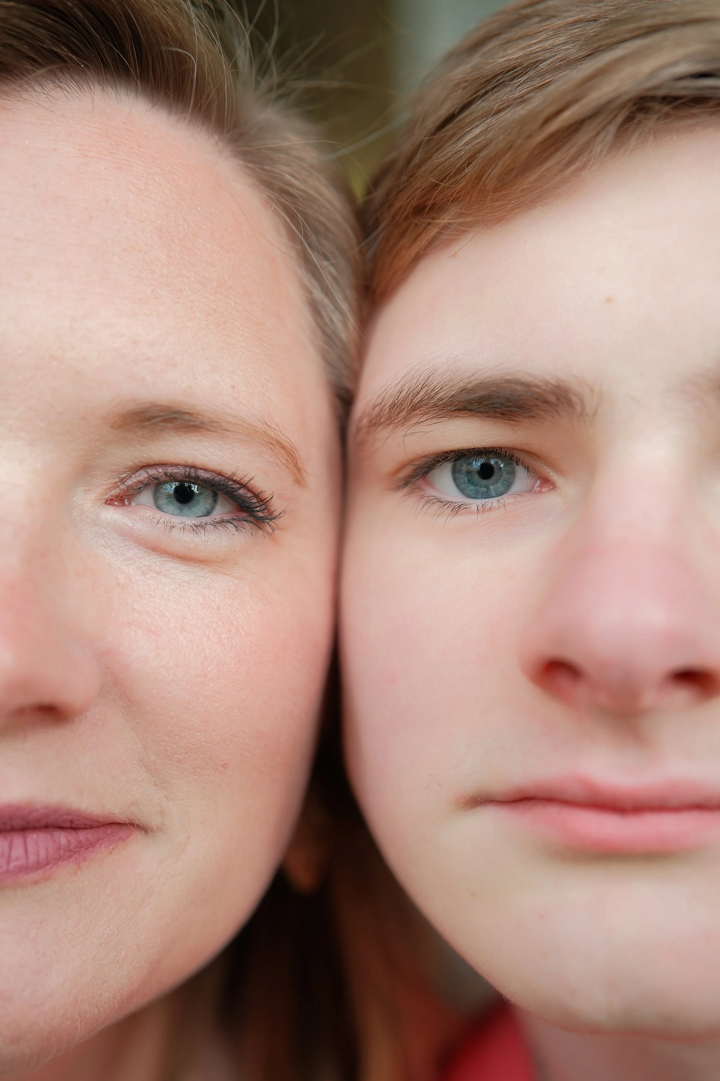Close-up of two people with blue eyes, closely positioned with their faces touching, showing detailed skin textures and brown and blonde hair.