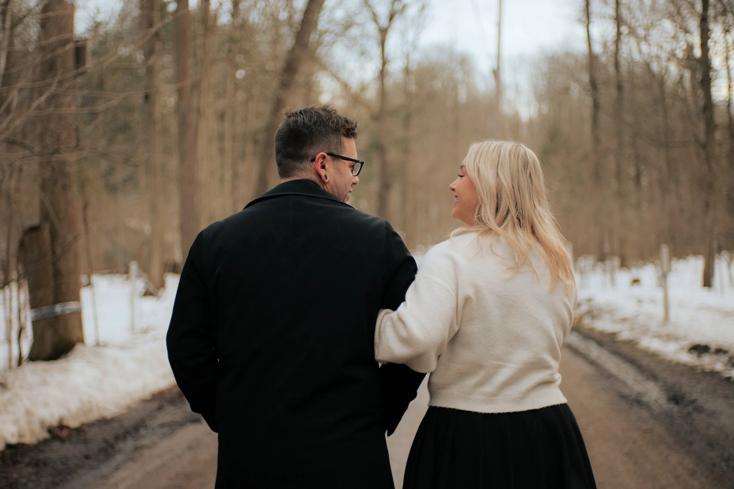 A couple holding hands and smiling at each other outdoors in a park during winter.