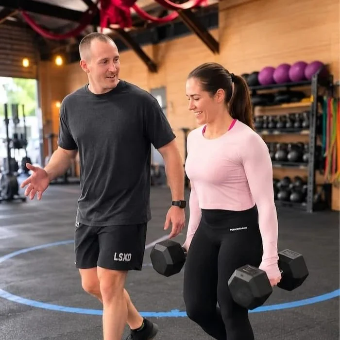 Dr Josh Saxton guiding a woman through a dumbbell carry during strength rehabilitation in Adelaide.